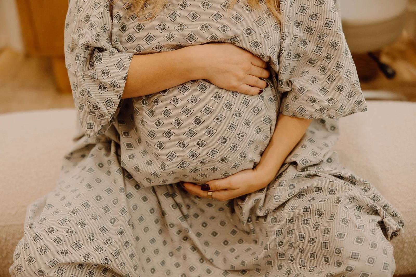 Pregnant patient in floral maternity dress cradling belly, seated pose — prenatal chiropractic care in Tulsa, Oklahoma