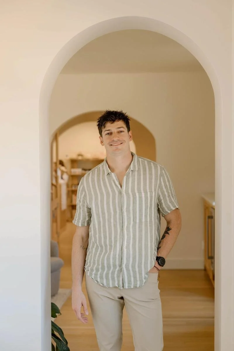 Dr. Colten Nevel portrait standing in striped olive shirt beneath office archway — Free Spirit Chiropractic of Tulsa, Oklahoma