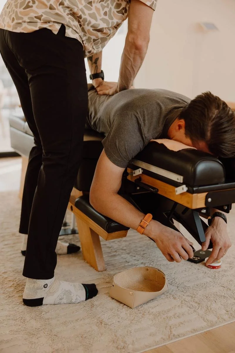 Male patient in prone position receiving lumbar adjustment with practitioner in striped shirt — adult chiropractic adjustment in Tulsa