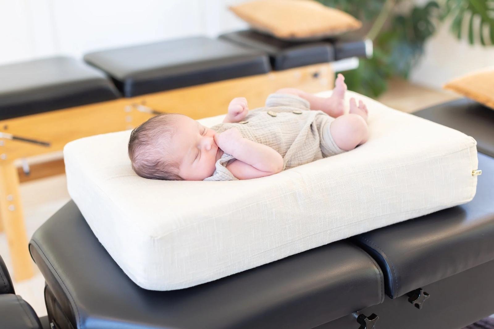 Calm baby in neutral romper resting on cream chiropractic support pillow — infant chiropractic care at Free Spirit Chiropractic in Tulsa