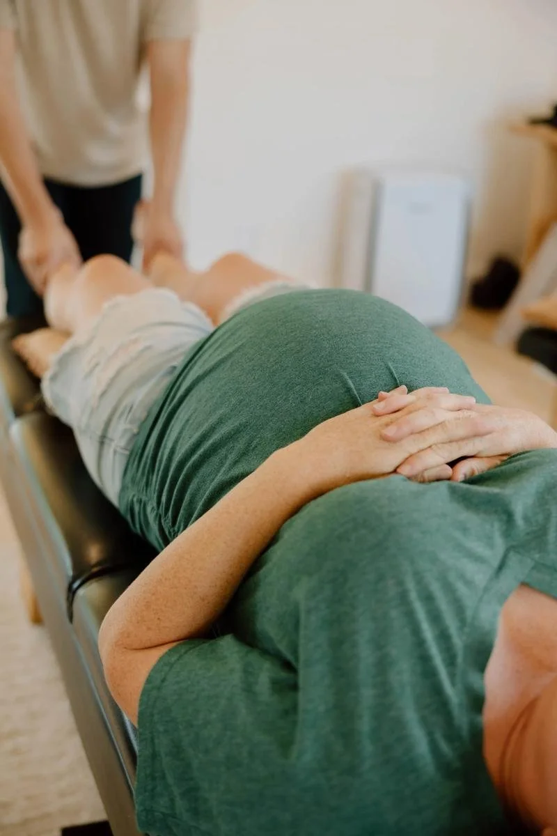 Pregnant patient in green top side-lying on table during Webster Technique pelvic balancing — prenatal chiropractic care in Tulsa, Oklahoma