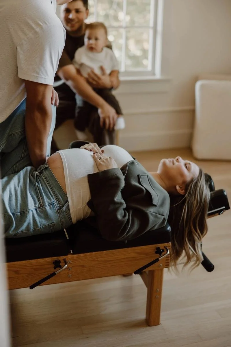 Pregnant patient receiving back adjustment on table while partner and toddler observe nearby — prenatal chiropractic care in Tulsa, Oklahoma