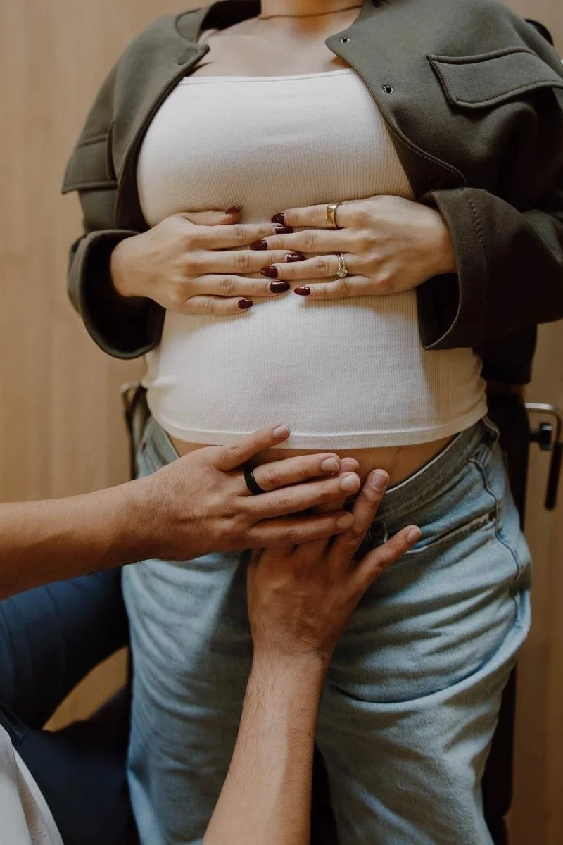 Hands gently holding pregnant belly during prenatal assessment, patient in green jacket — prenatal chiropractic care in Tulsa, Oklahoma