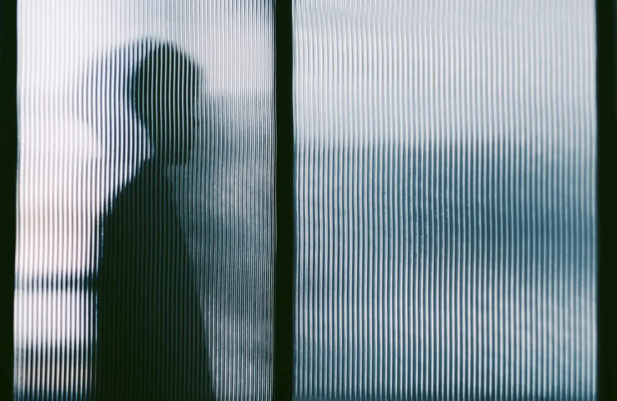 A blurry silhouette stands behind a frosted, ribbed glass window—like viewing users through a client portal for web designers.