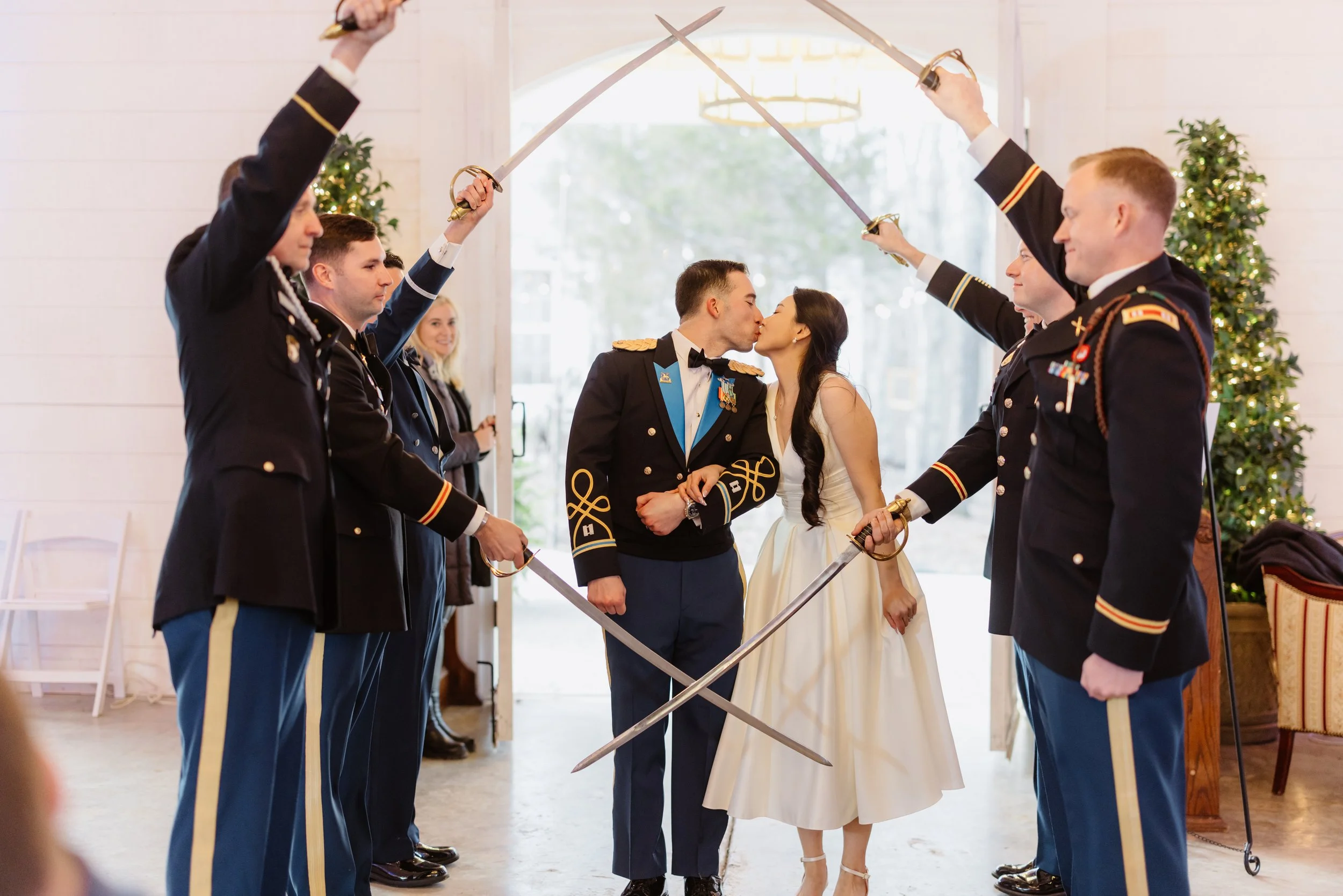 A military couple kissing during their wedding ceremony while surrounded by soldiers forming an arch with swords.