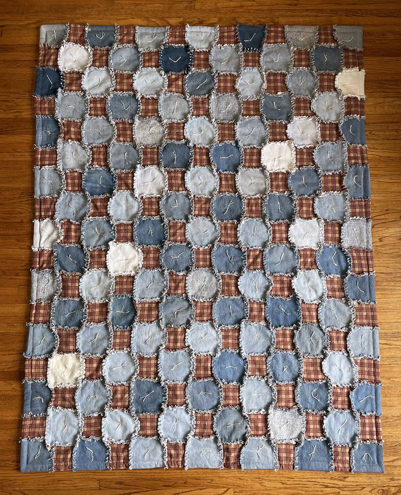 Denim Patchwork, Comforter, Twin, 60x76: Tammy Riedel, First Mennonite, Lincoln

An upcycled denim blanket with burgundy and tan plaid flannel in a patchwork pattern. It is backed with a brown flannel and tied.