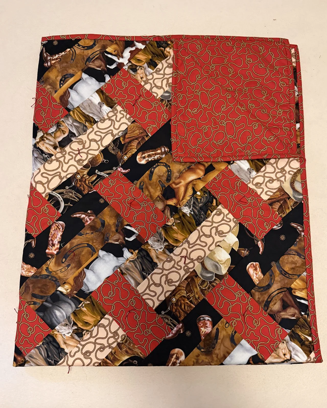 Horsing Around, Comforter, Lap/Throw, 44x54: Kathy Boshart, First Mennonite, Lincoln

This diagonal rail quilt is made with horse and rope prints in brown, tan, and red, with a backing of a twisted rope in red. It was pieced and tied by Kathy Boshart