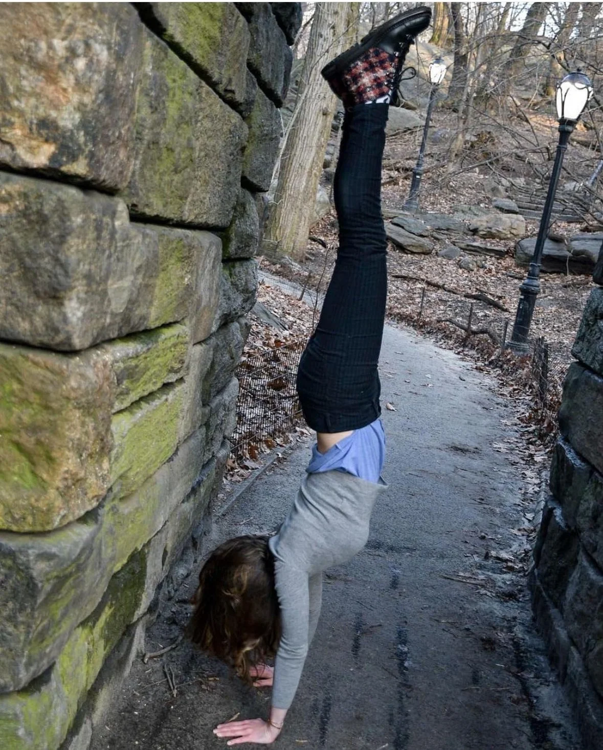 Person performing a handstand against stone walls on a park path in winter.