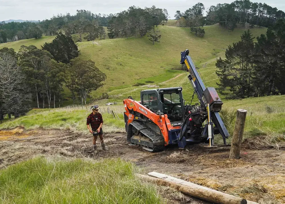 operator using remote control skidsteer mounted post driver on a steep hillside