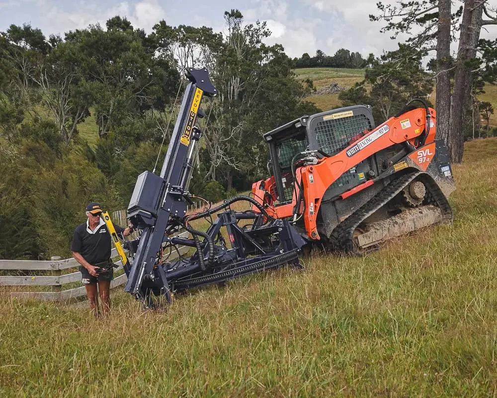 Revolution Swinga post driver on a Kubota skid steer fencing on green farmland with operator