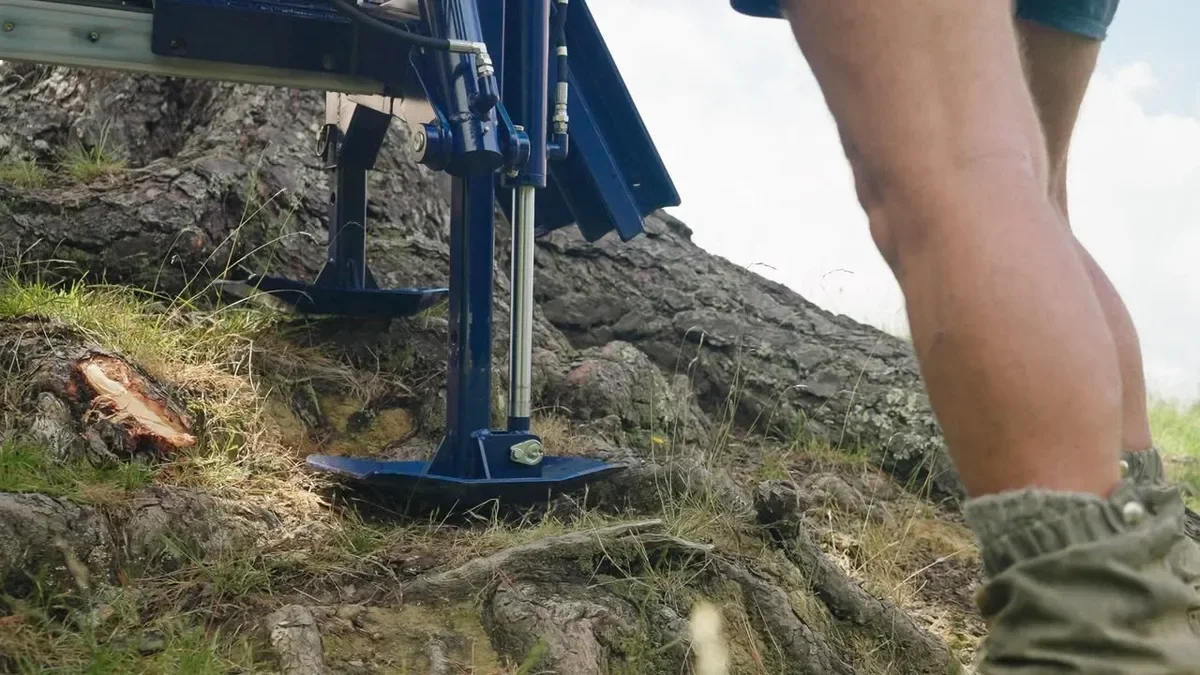 Close-up of Revolution post driver hydraulic foot on tree roots covered hillside