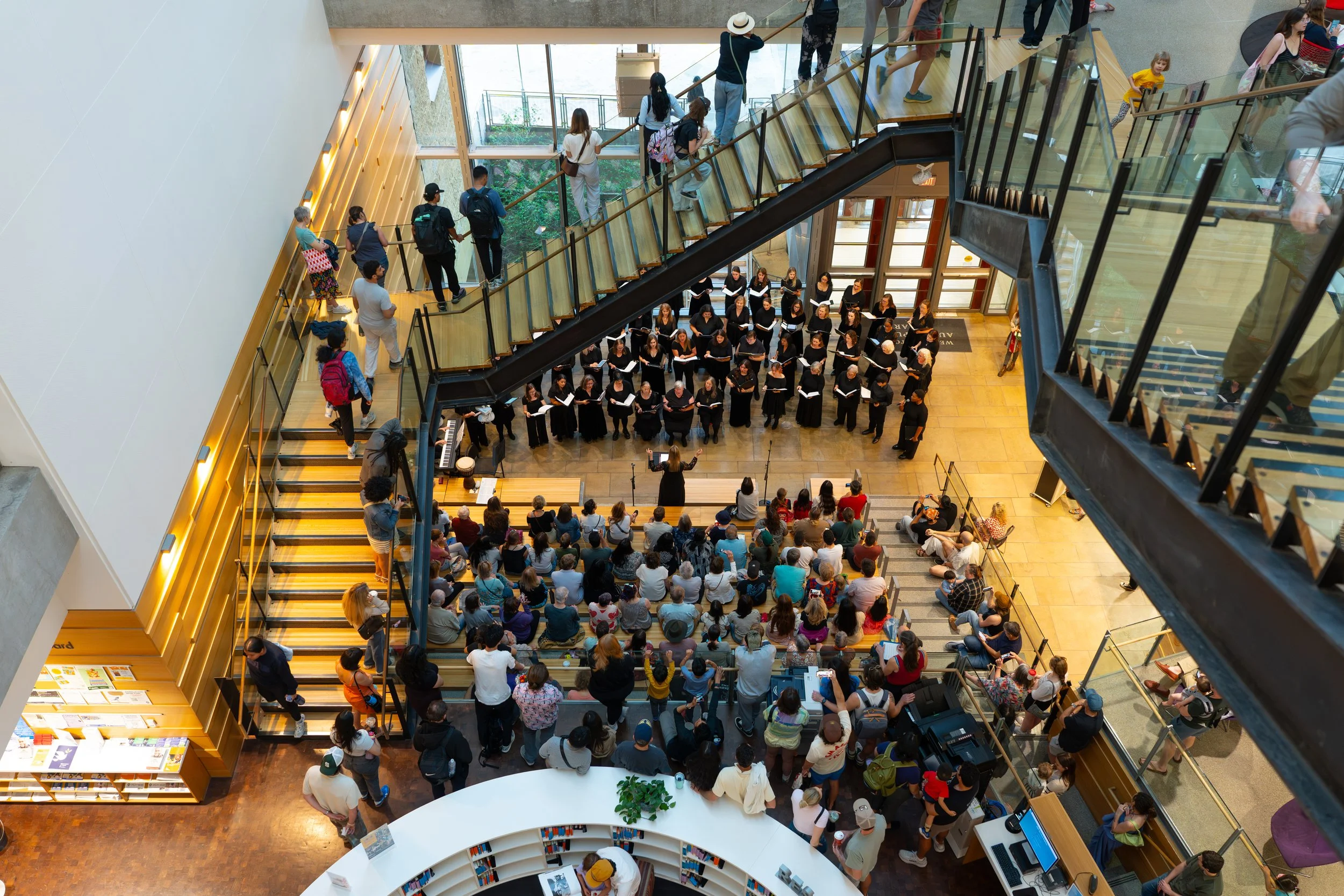 SoCo Women’s Chorus performs in black attire for a seated audience at Austin Central Library atrium.