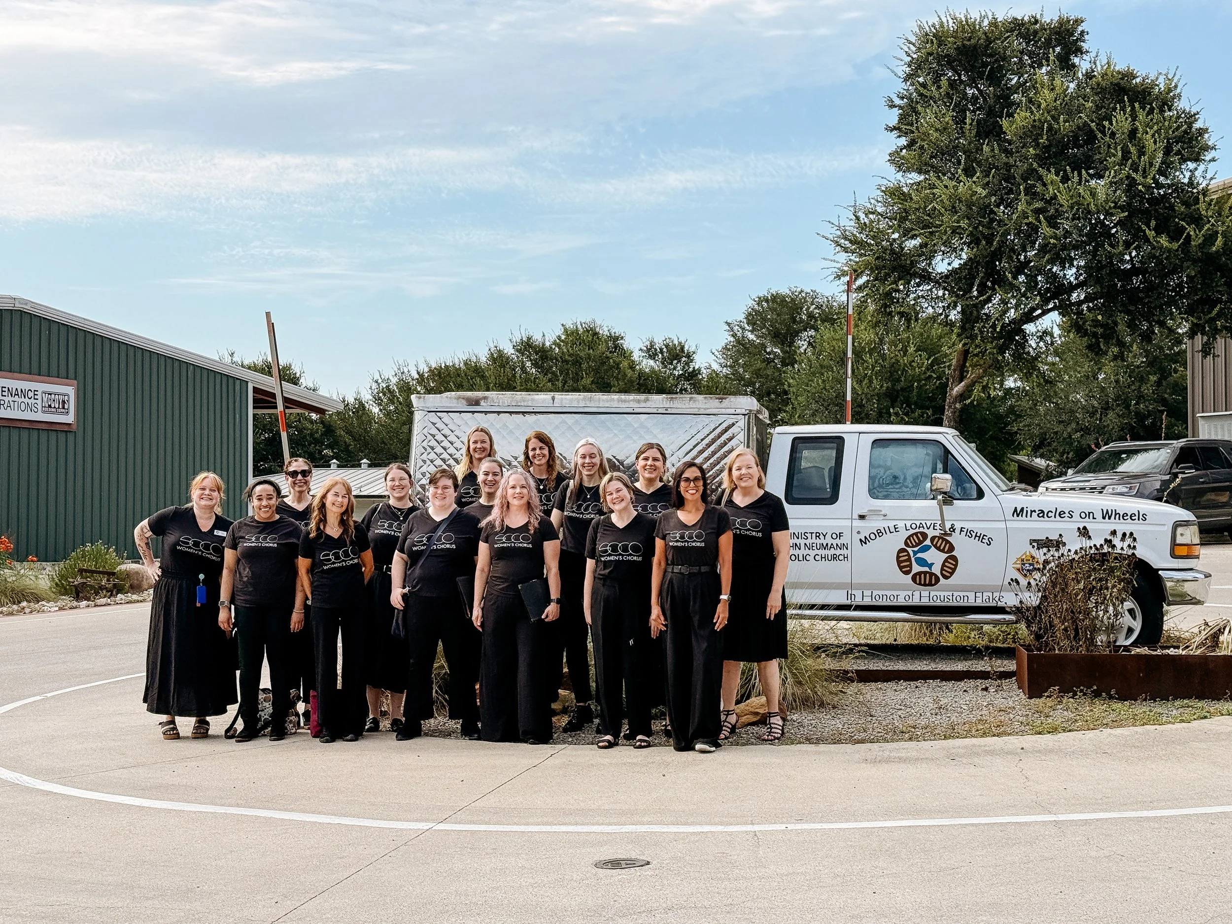 A group of SoCo Women’s Chorus singers poses outdoors beside a Mobile Loaves & Fishes “Miracles on Wheels” truck.