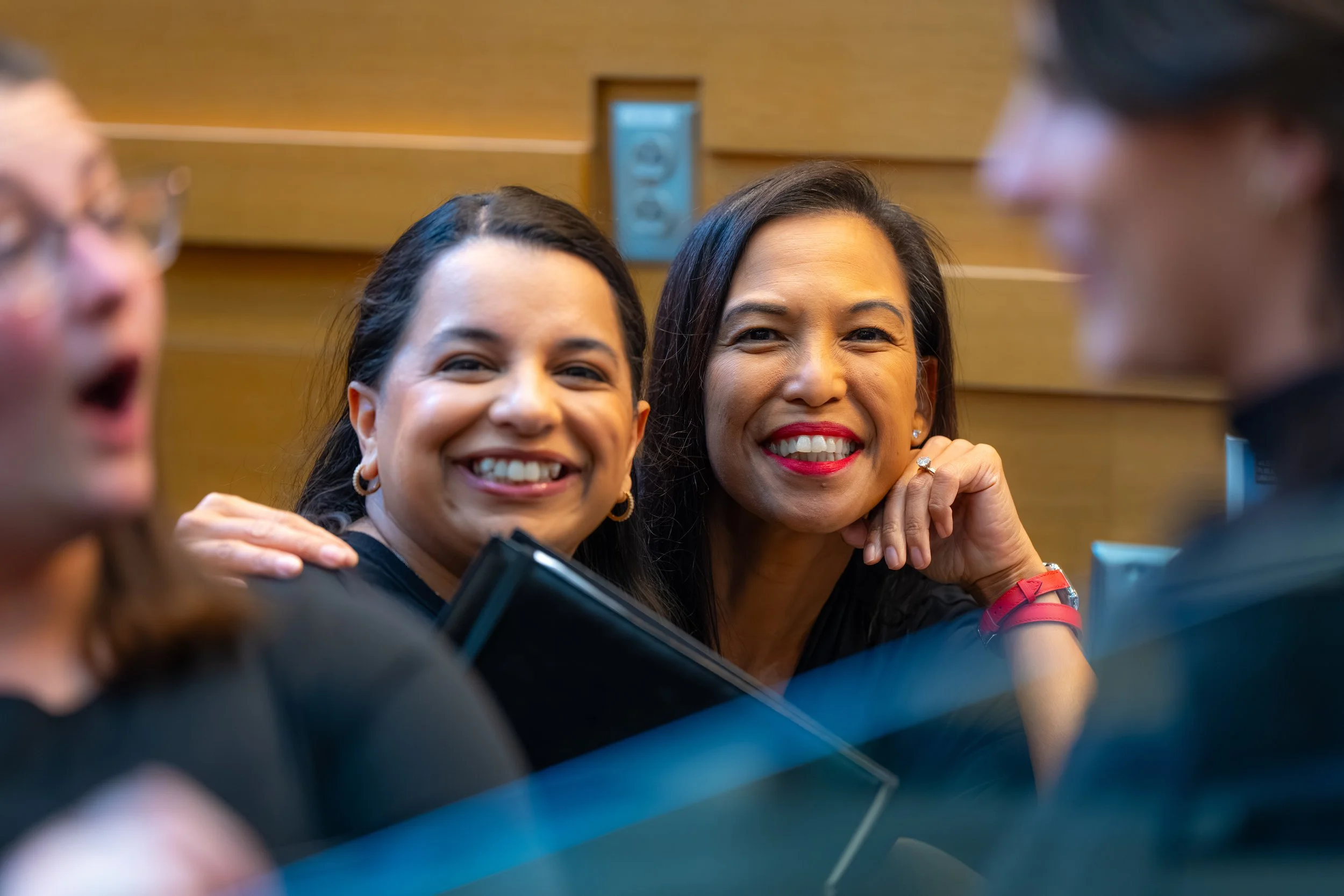 Two smiling SoCo Women’s Chorus members pose closely before a concert, holding black folders.