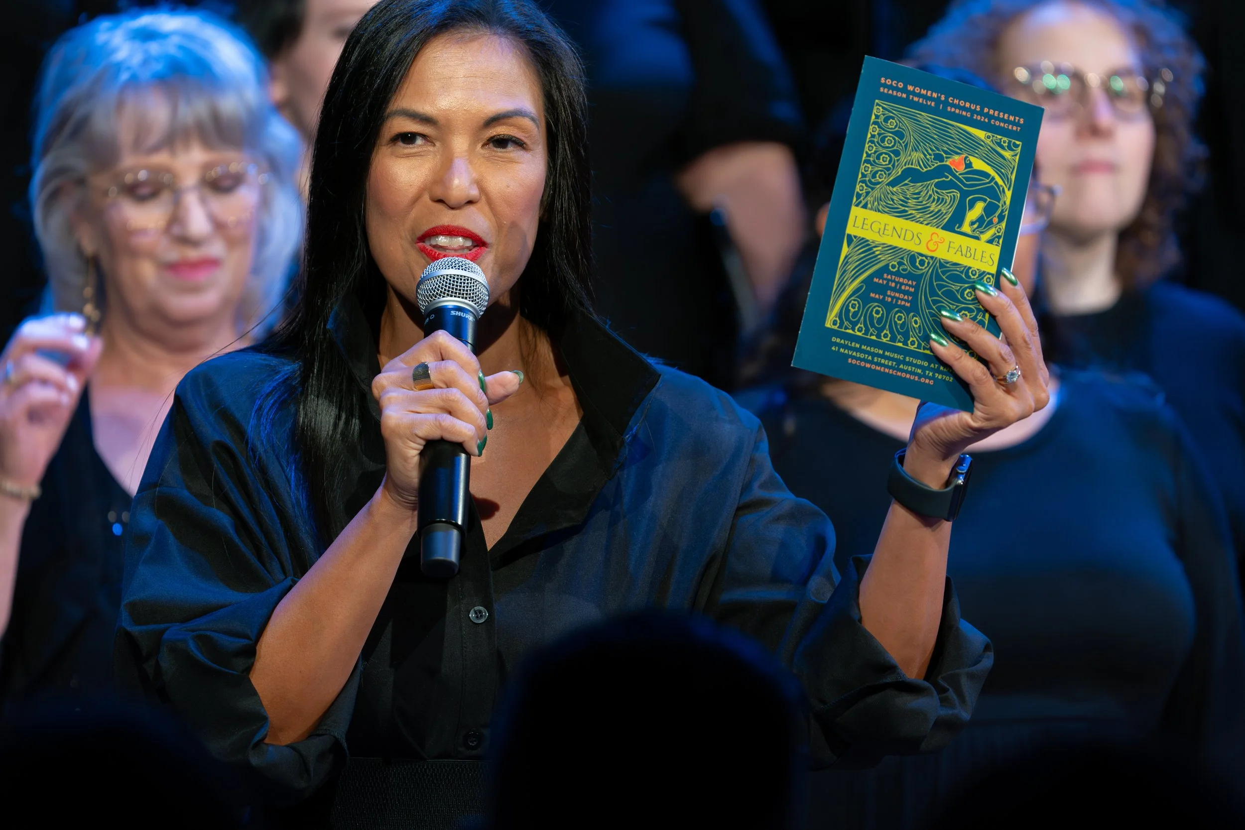 Speaker holding microphone and displaying a playbill during concert with choir in background