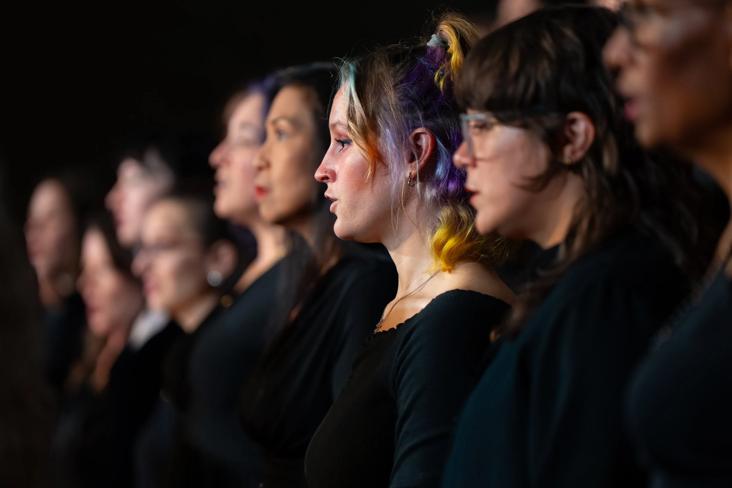 Close-up profile view of choir members singing during a concert, dressed in black.