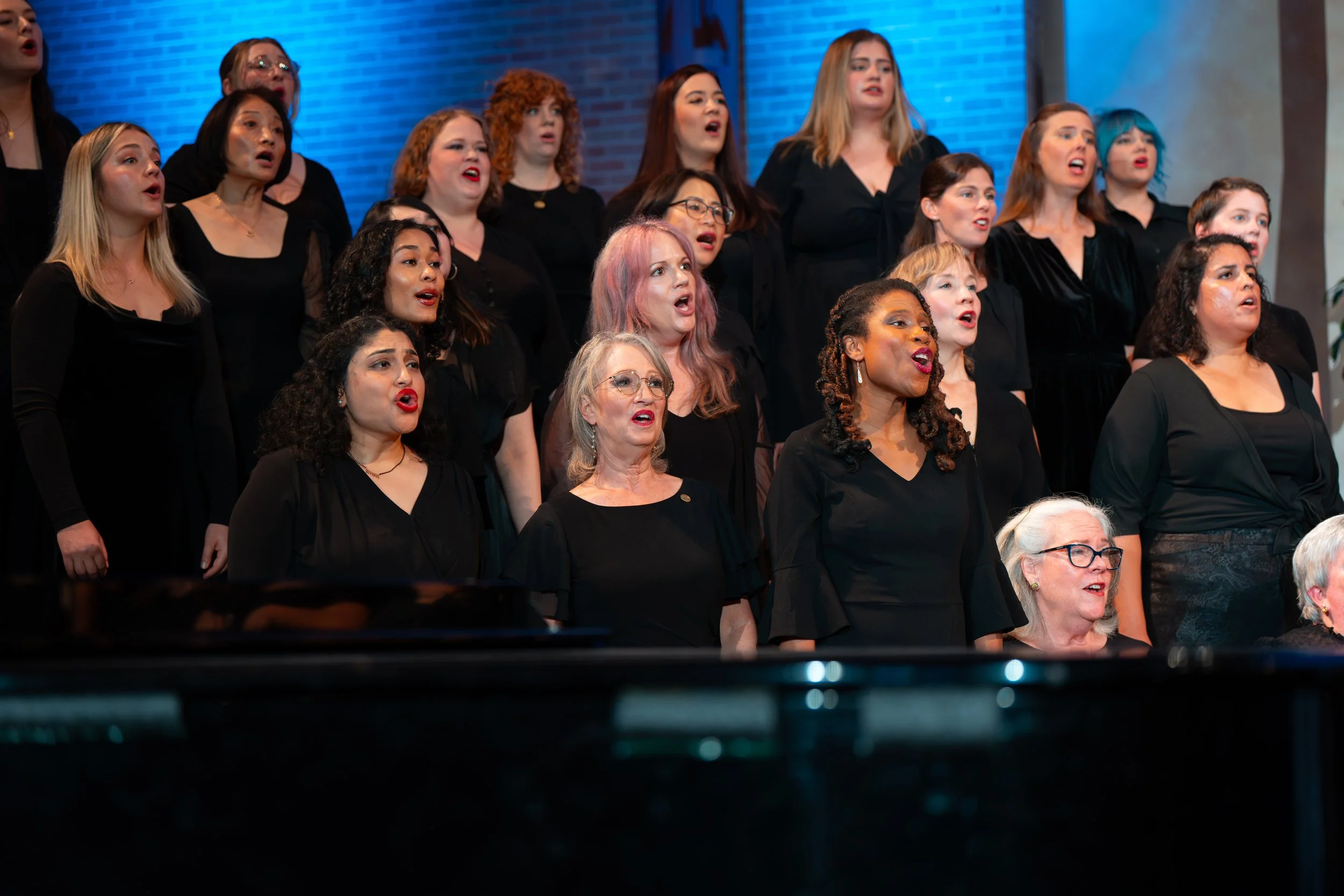A group of women singing on stage in formal black attire during a choral performance.