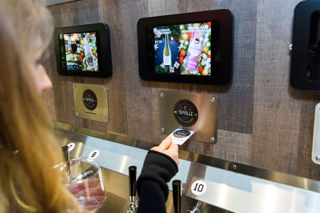 Person purchasing a bottled beverage using a self-service vending kiosk at Tapville.