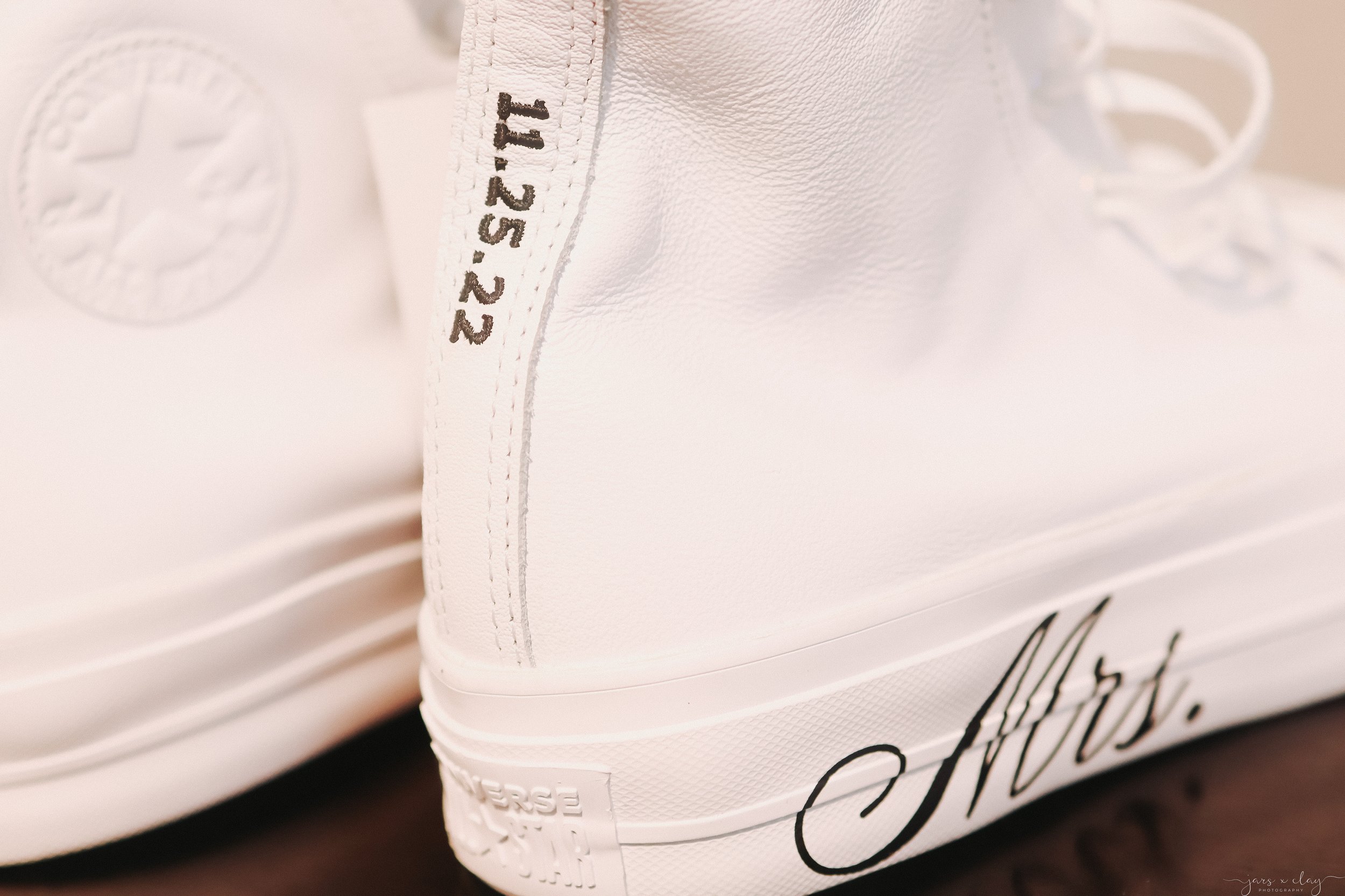 Close-up of a white sneaker with visible stitching and black text on the side and heel.