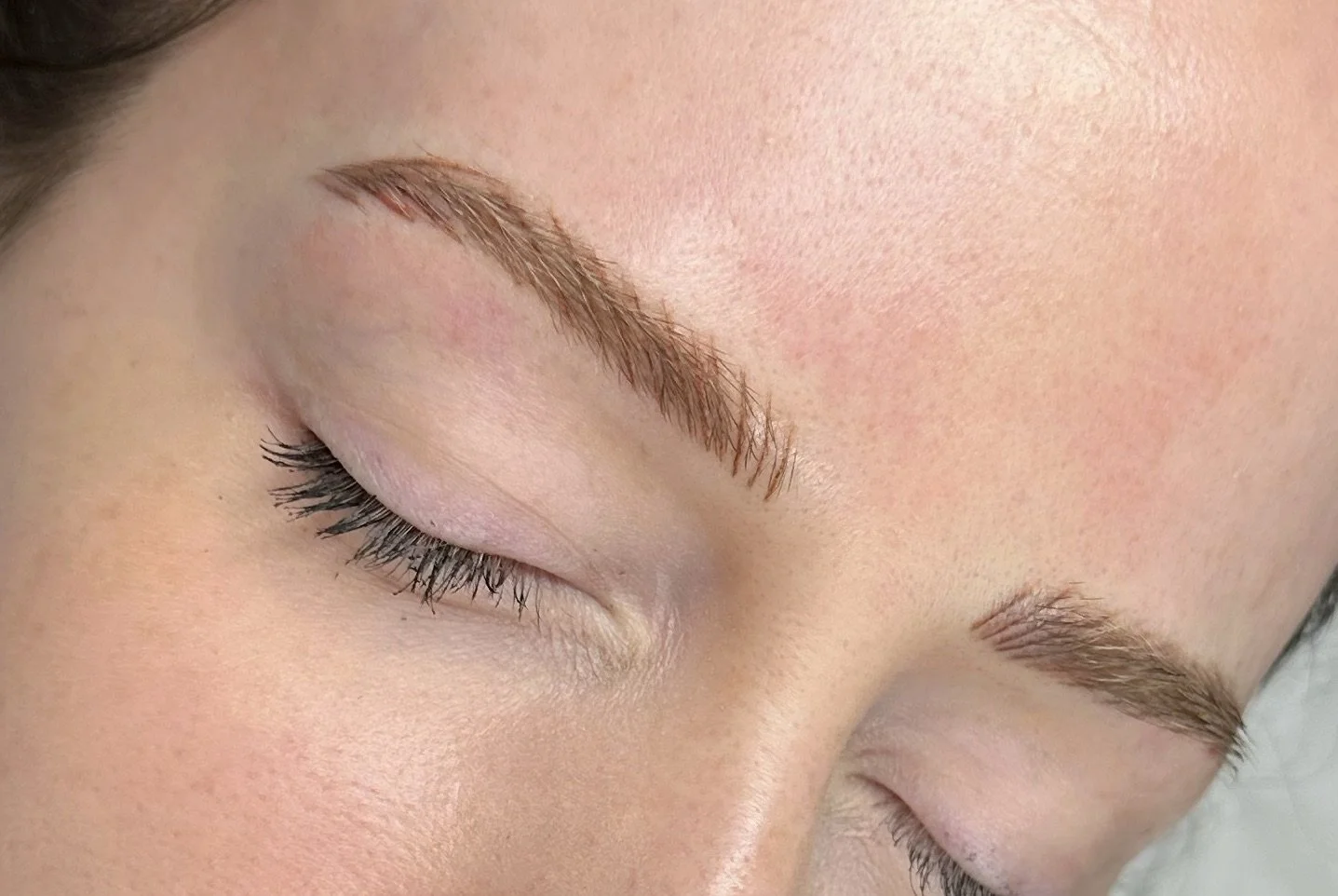 Close-up of a person's face with closed eyes, showing well-groomed eyebrows and long eyelashes.