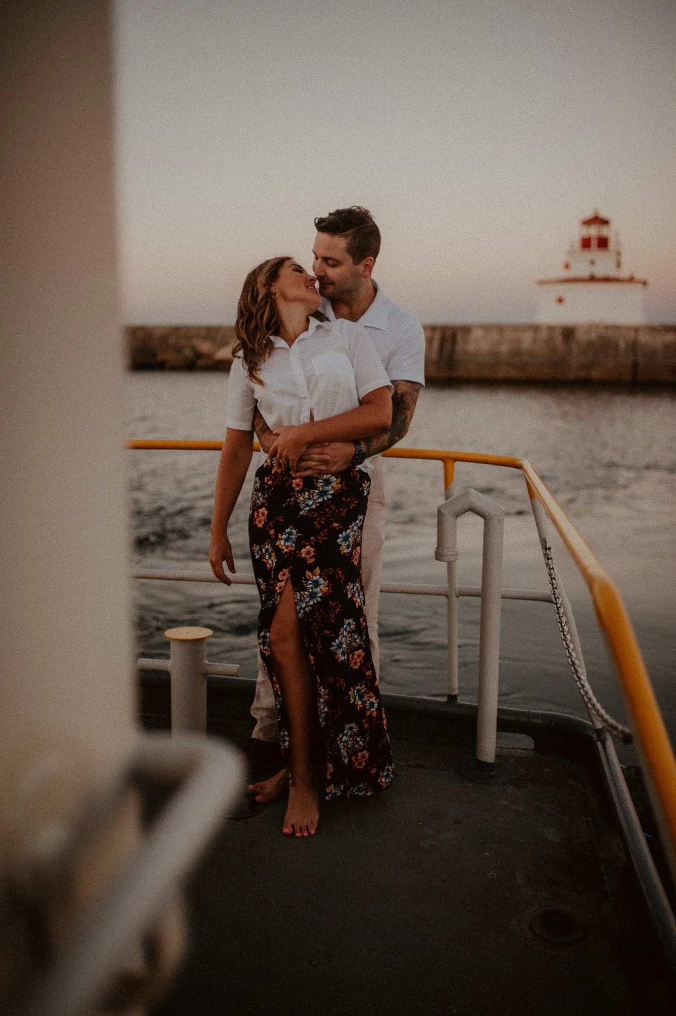 A couple embracing on a boat at sunset with a lighthouse in the background in Port Colborne, Ontario.