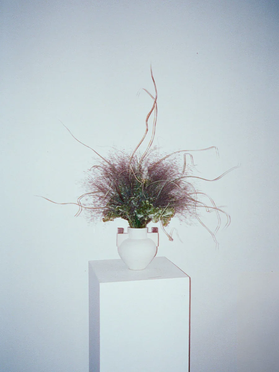 Modern dried floral arrangement in a white ceramic vase on a pedestal against a minimalist wall