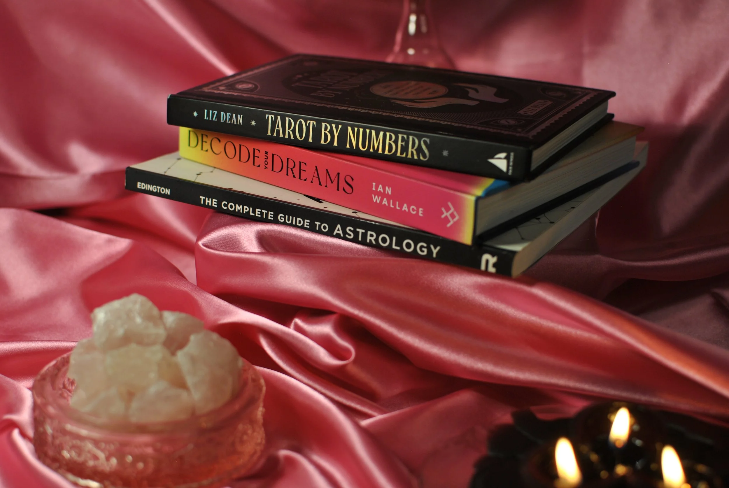 rose quartz is arranged with a pink, satin backdrop and three books for self exploration. "tarot by numbers," "decode your dreams," and, "the complete guide to astrology."