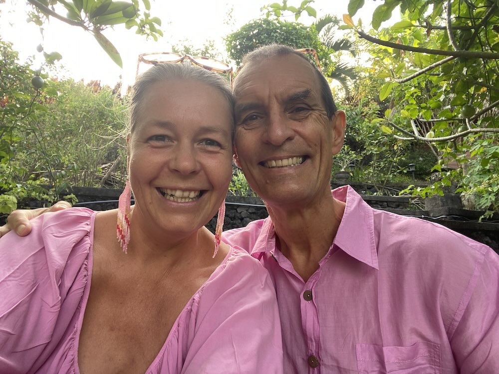 Anastasia und Christian Kaesbach mit passenden rosafarbenen Hemden bei einem Selfie im Freien inmitten üppiger grüner Bäume.
