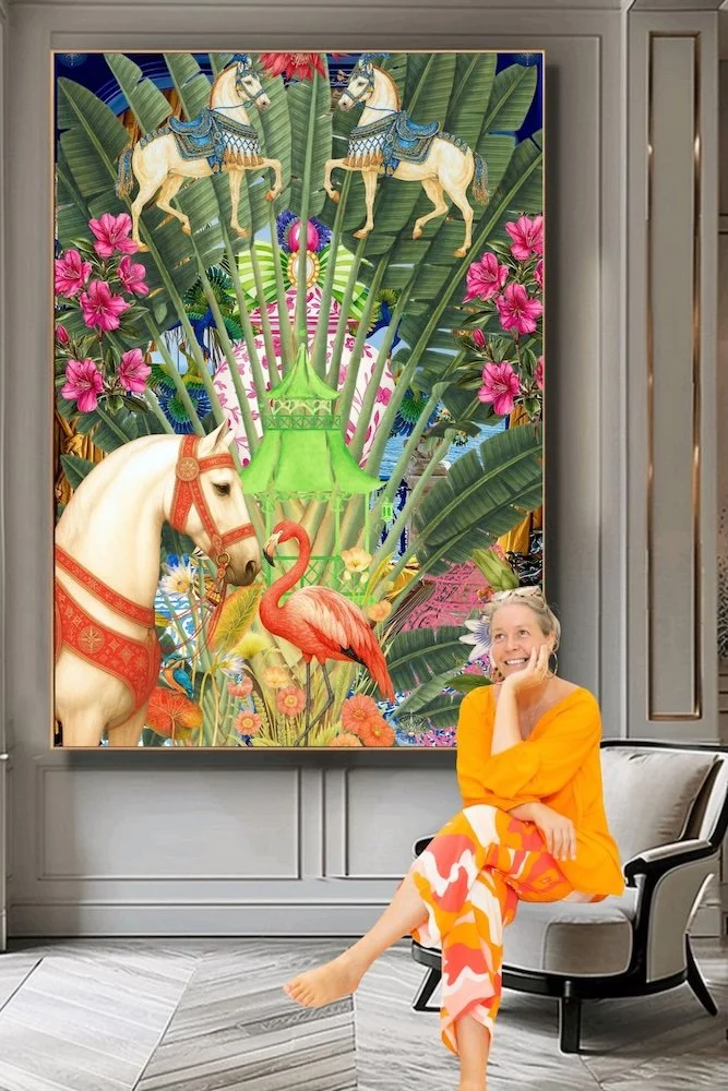 © Anastasia Kaesbach. Anastasia in an orange shirt and patterned pants sitting on a beige armchair in front of a colorful, vibrant painting featuring carousel horses, a flamingo, palm leaves, and pink flowers.