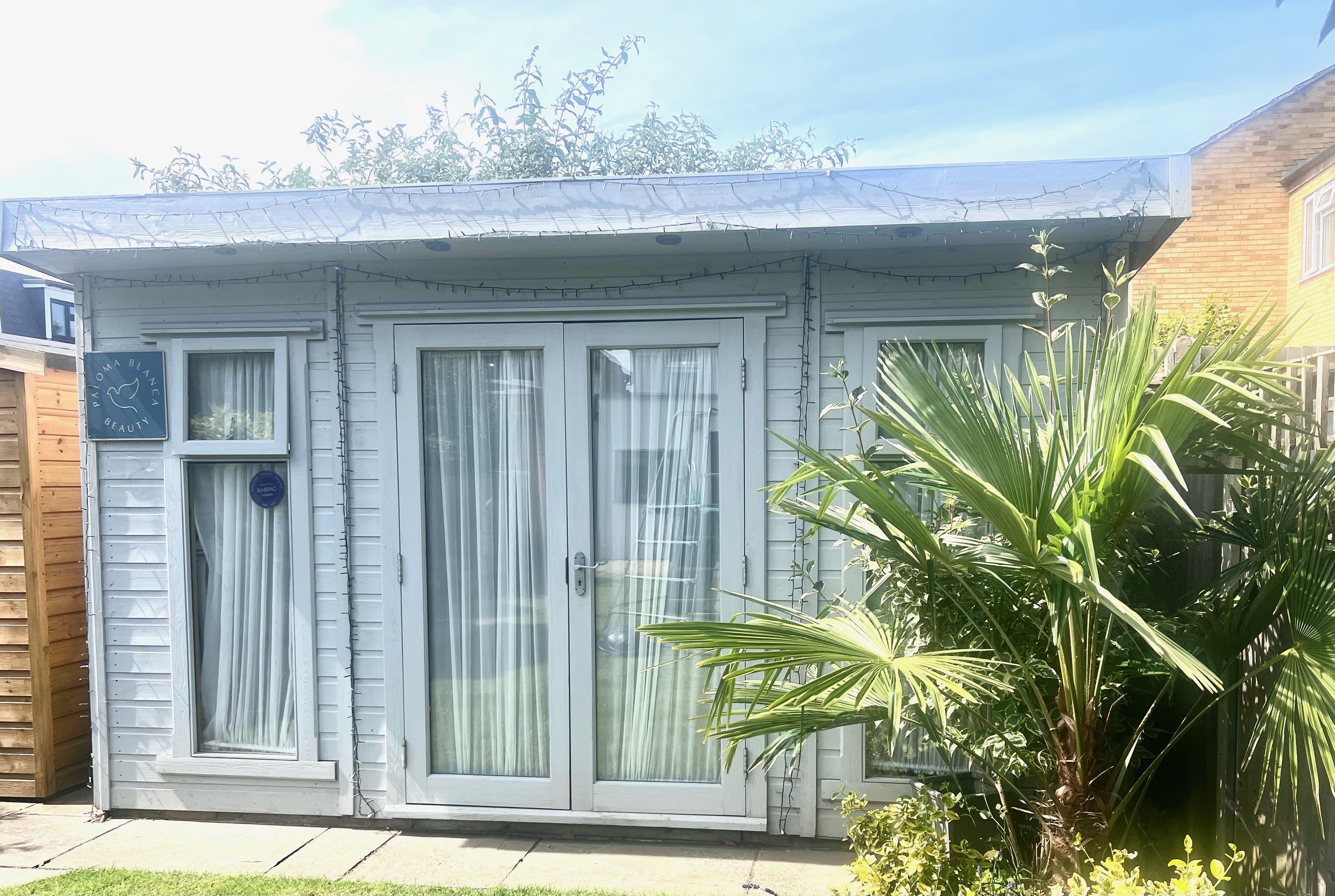 Small garden shed with glass doors, curtains, and plants outside