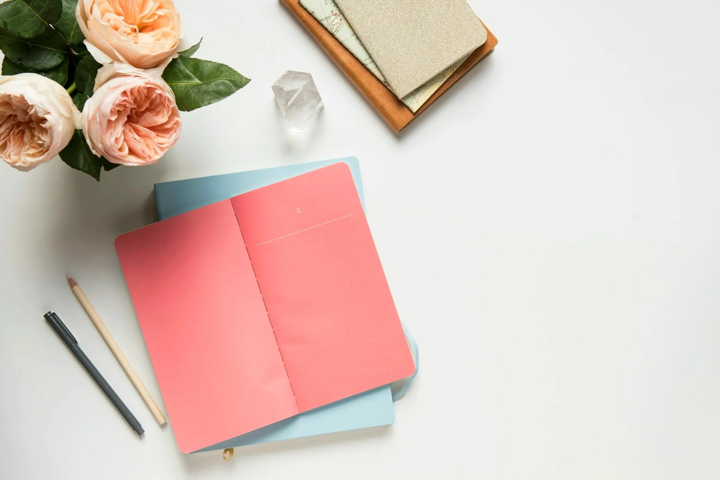 Bright pink notebook splayed open atop a white desk with pink flowers and two pens
