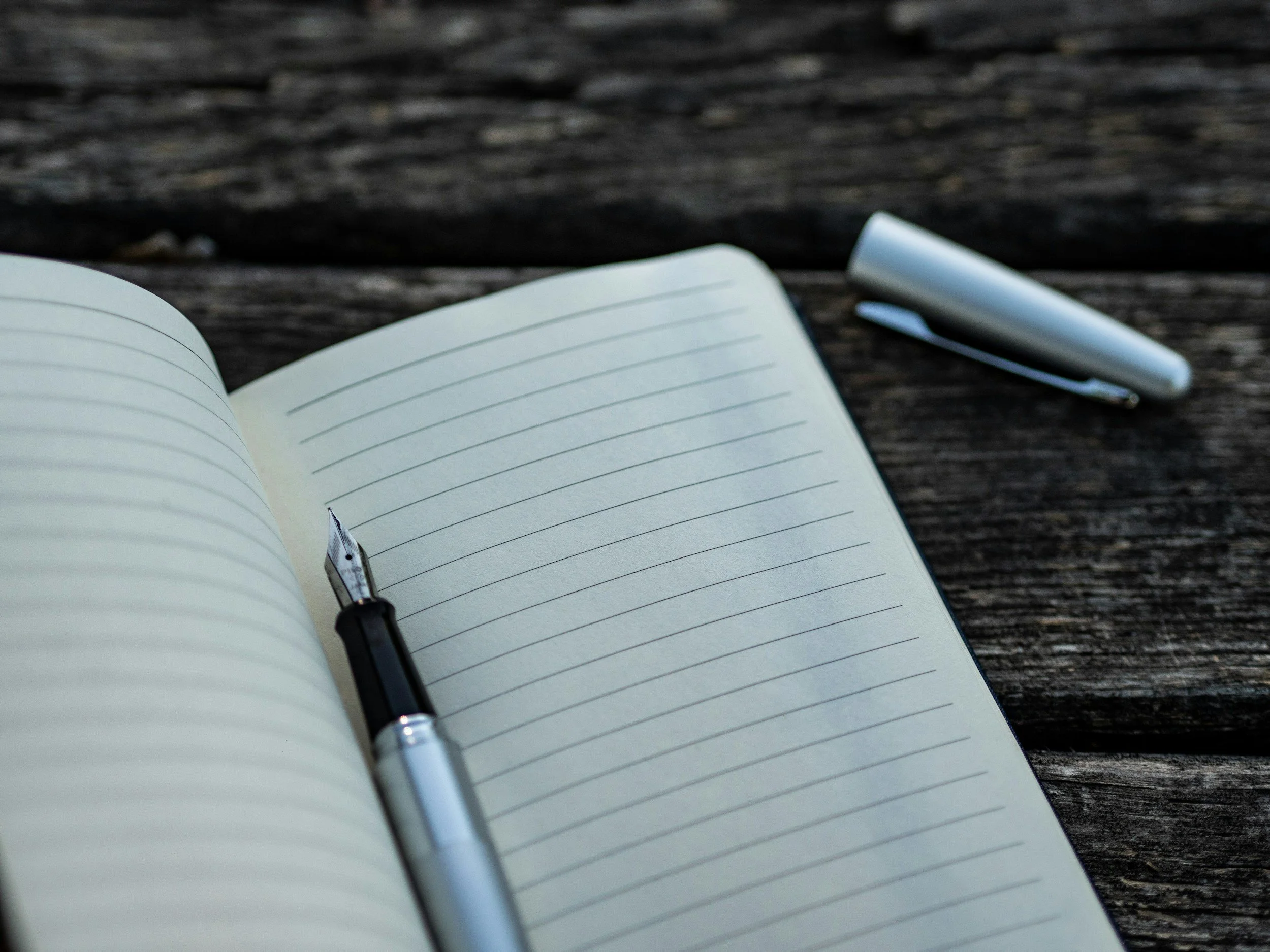 an open notebook to an empty lined page with an uncapped pen resting in the crease
