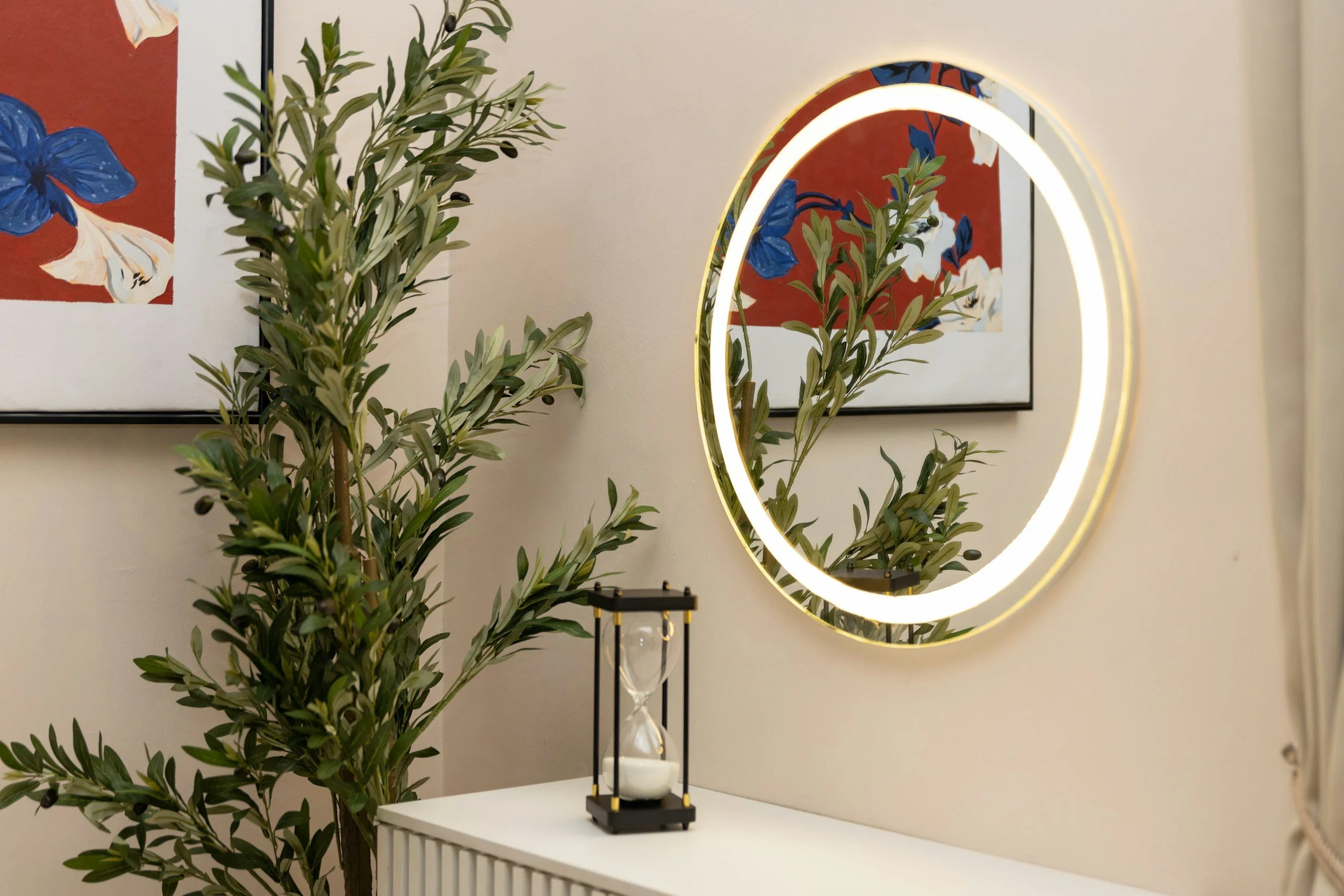 photo of a circular mirror hung above a white credenza next to a tall plant