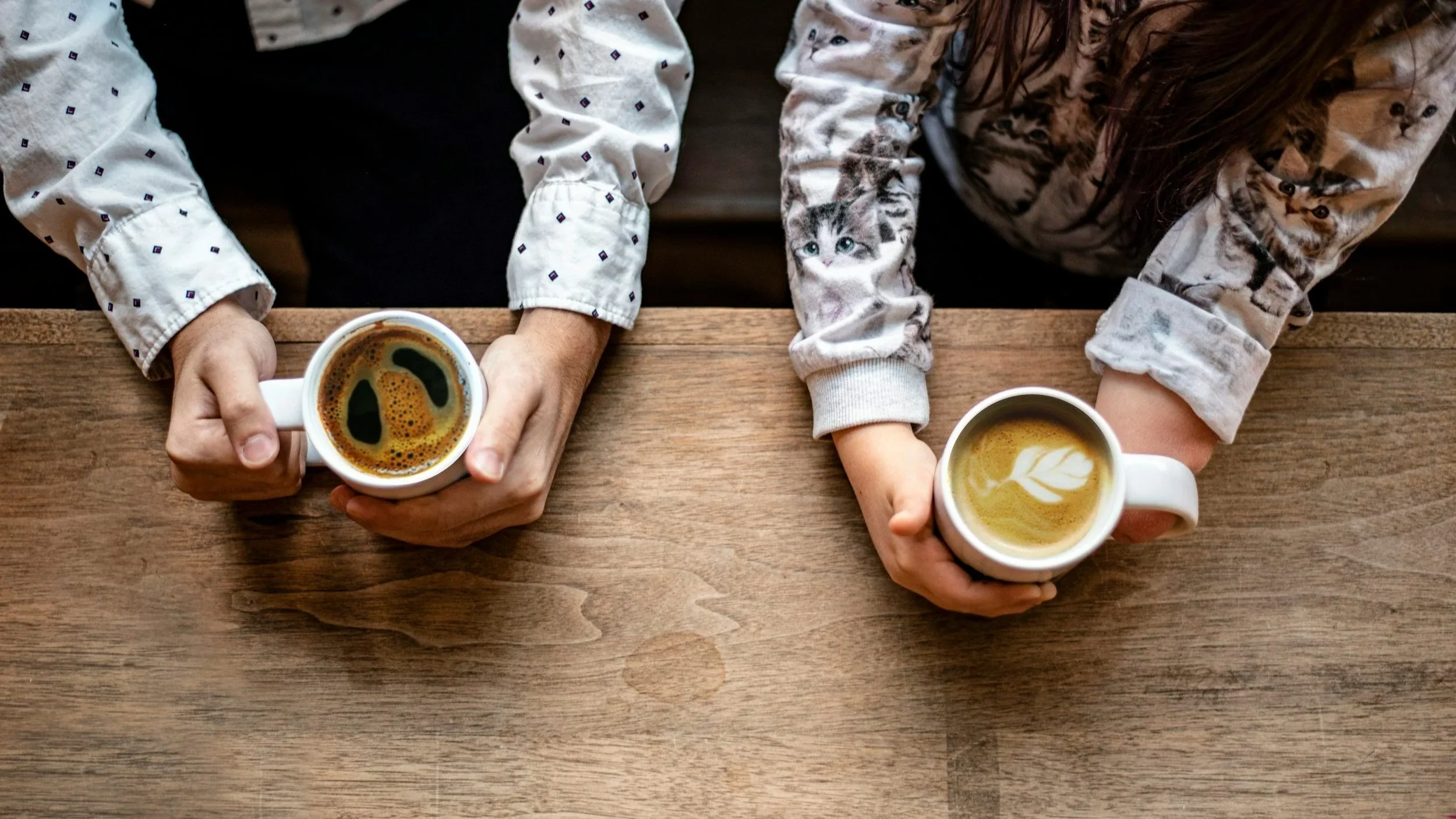 overhead image of two sets of arms and hands holding beverages, in the midst of a conversation