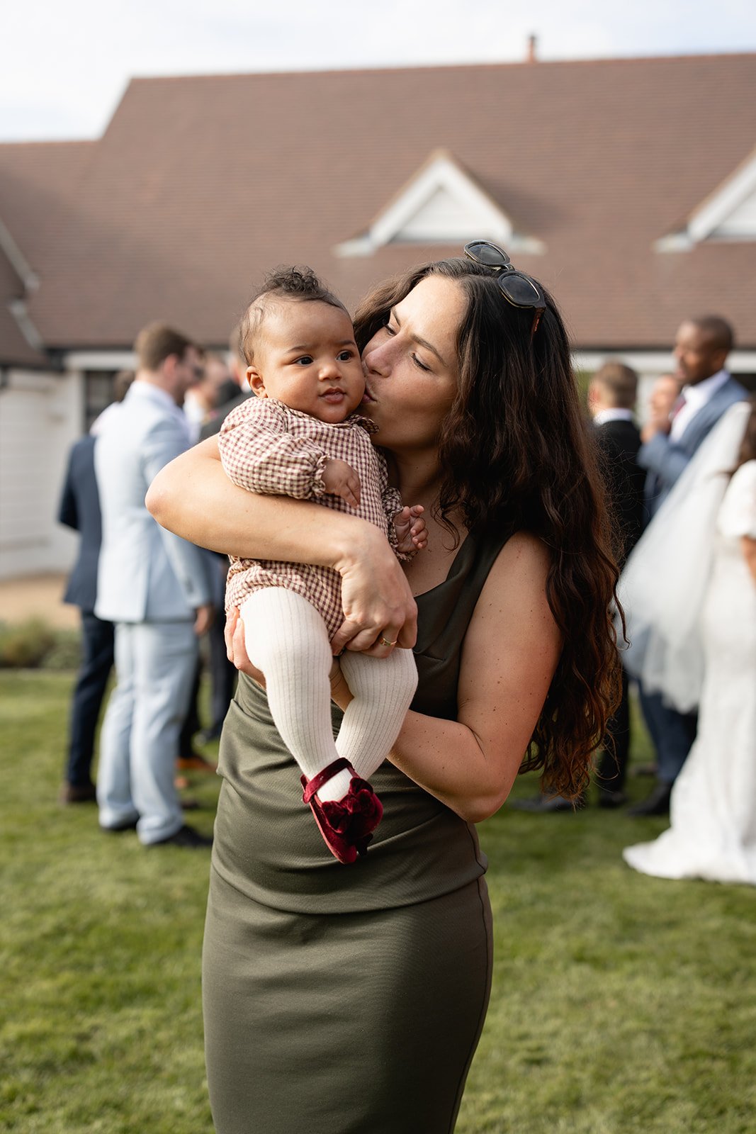 A woman holding a young child at an outdoor gathering with other people in the background.