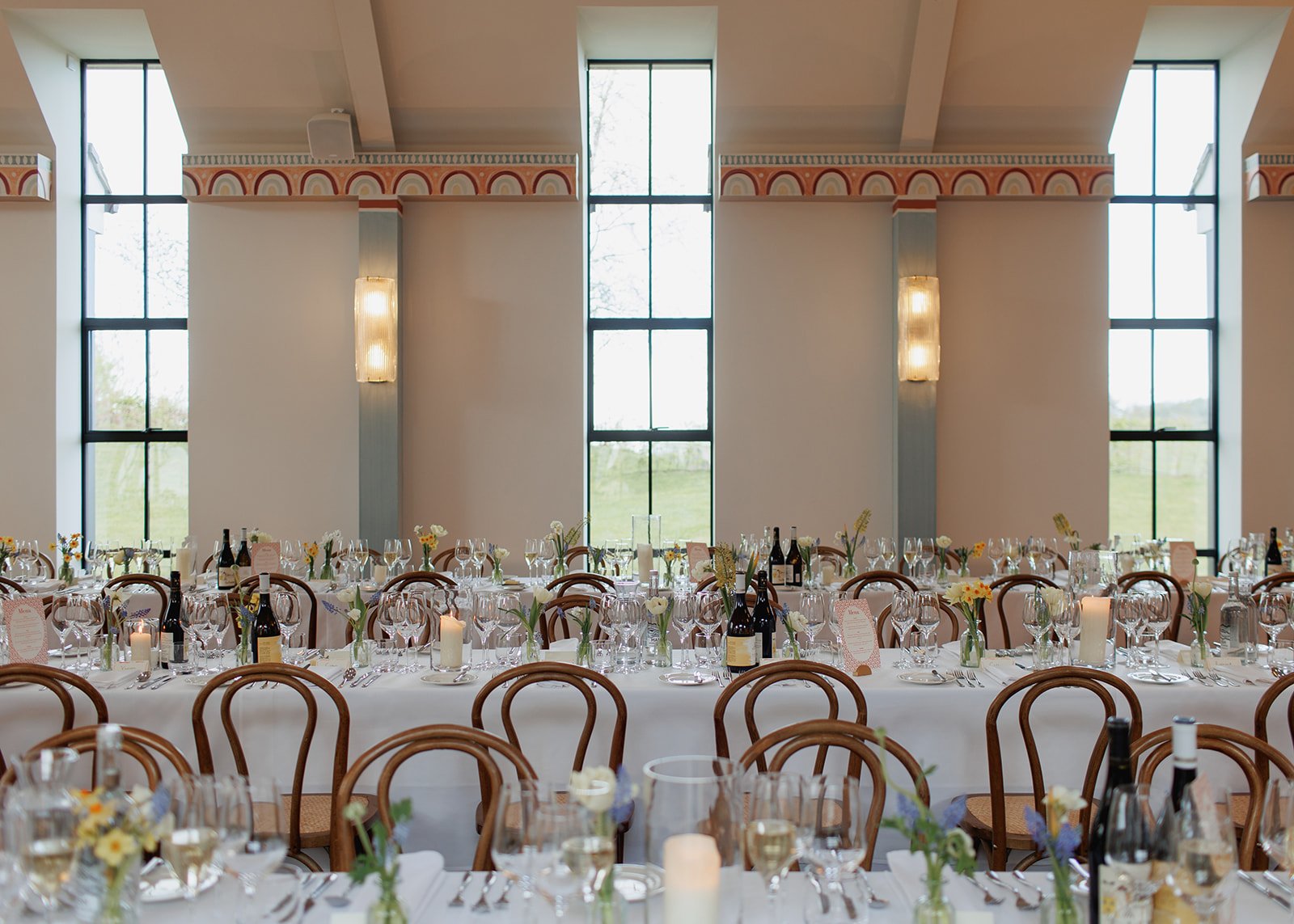 Elegant set up at LIMEKILN for a wedding, with long tables, floral centerpieces, candles, and wine bottles, large windows with natural light.