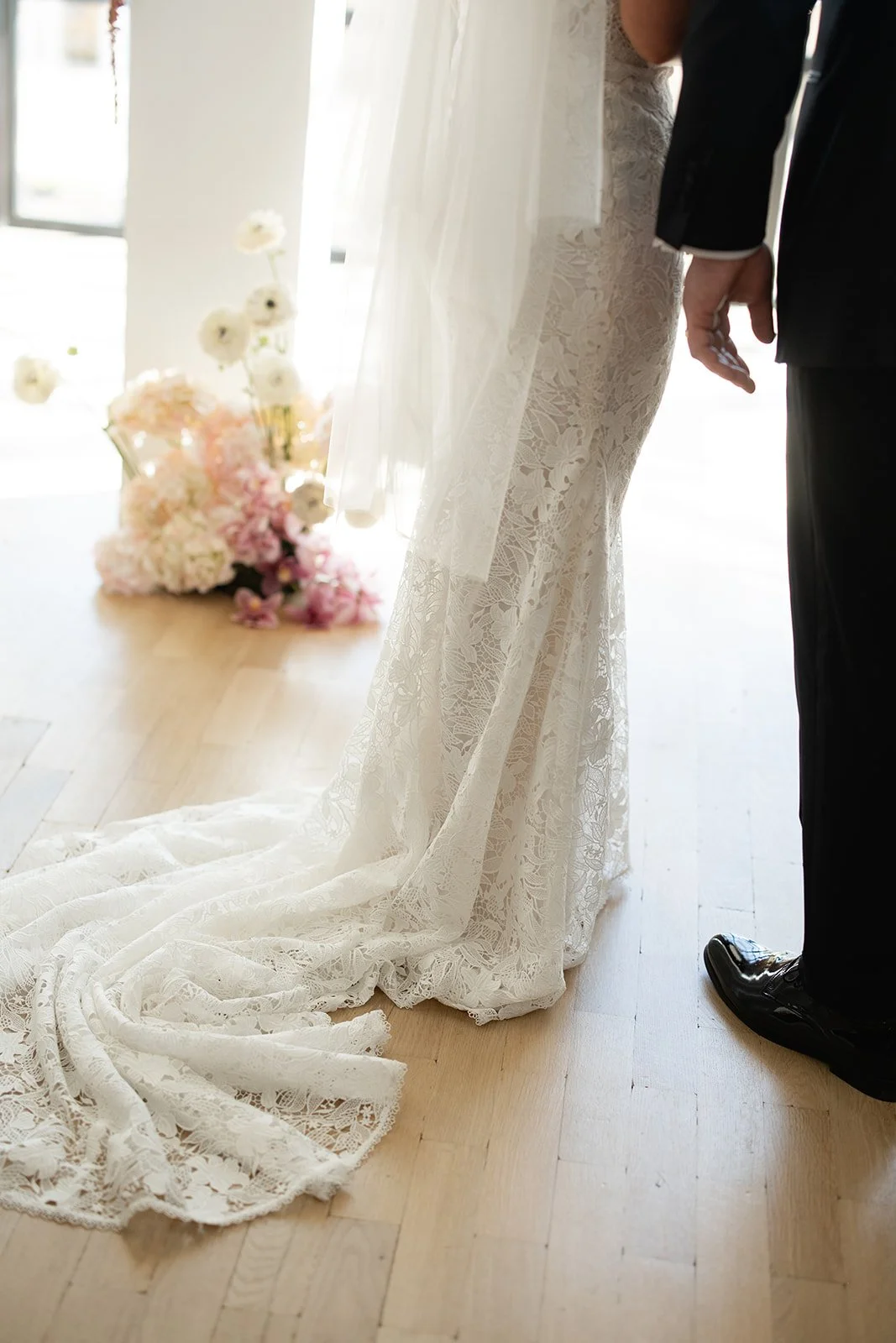 Close-up of a bride and groom holding hands during a wedding ceremony, with a bouquet of flowers on the floor in the background.