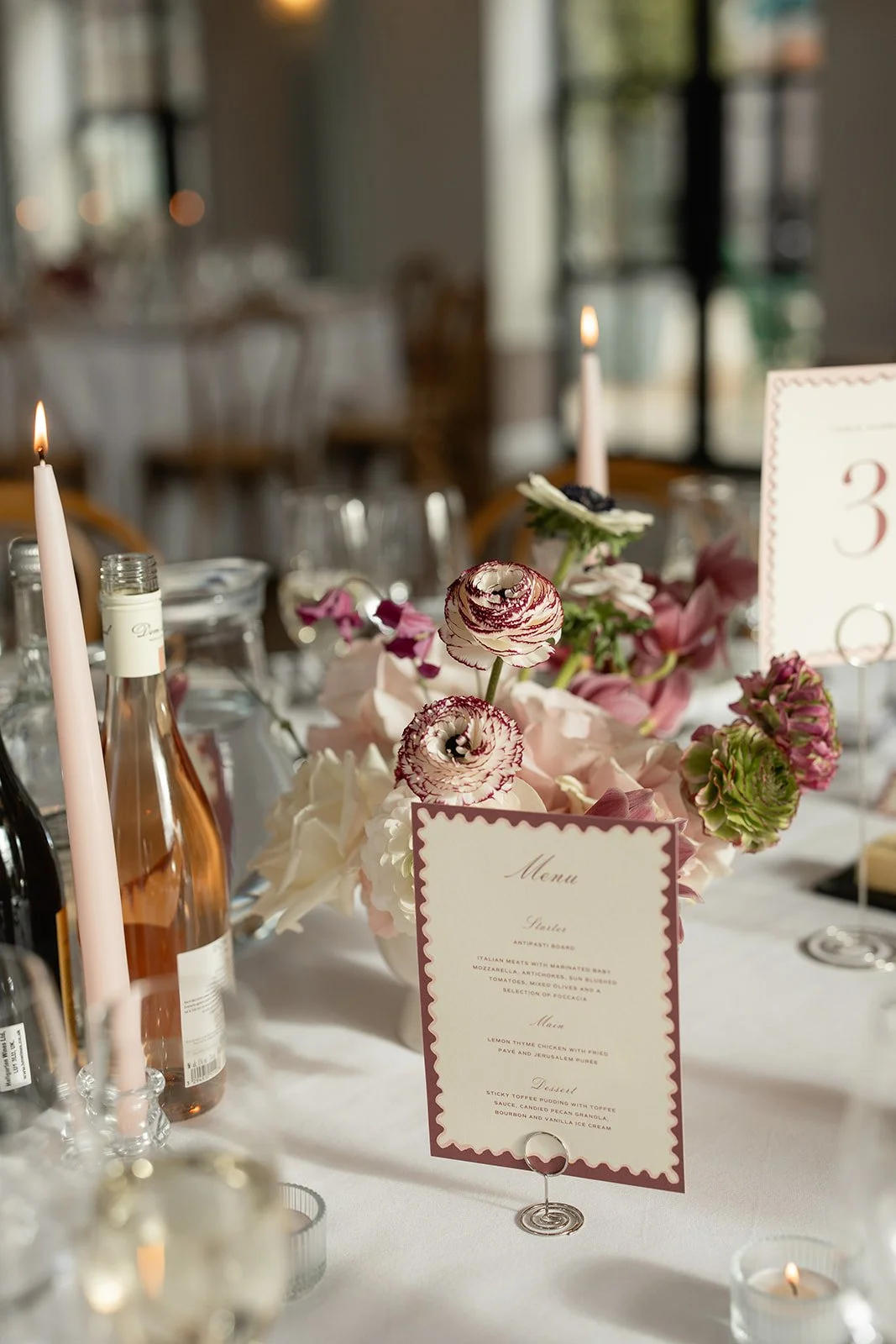 A wedding table centerpiece with pink and white flowers, candles, and a menu card.