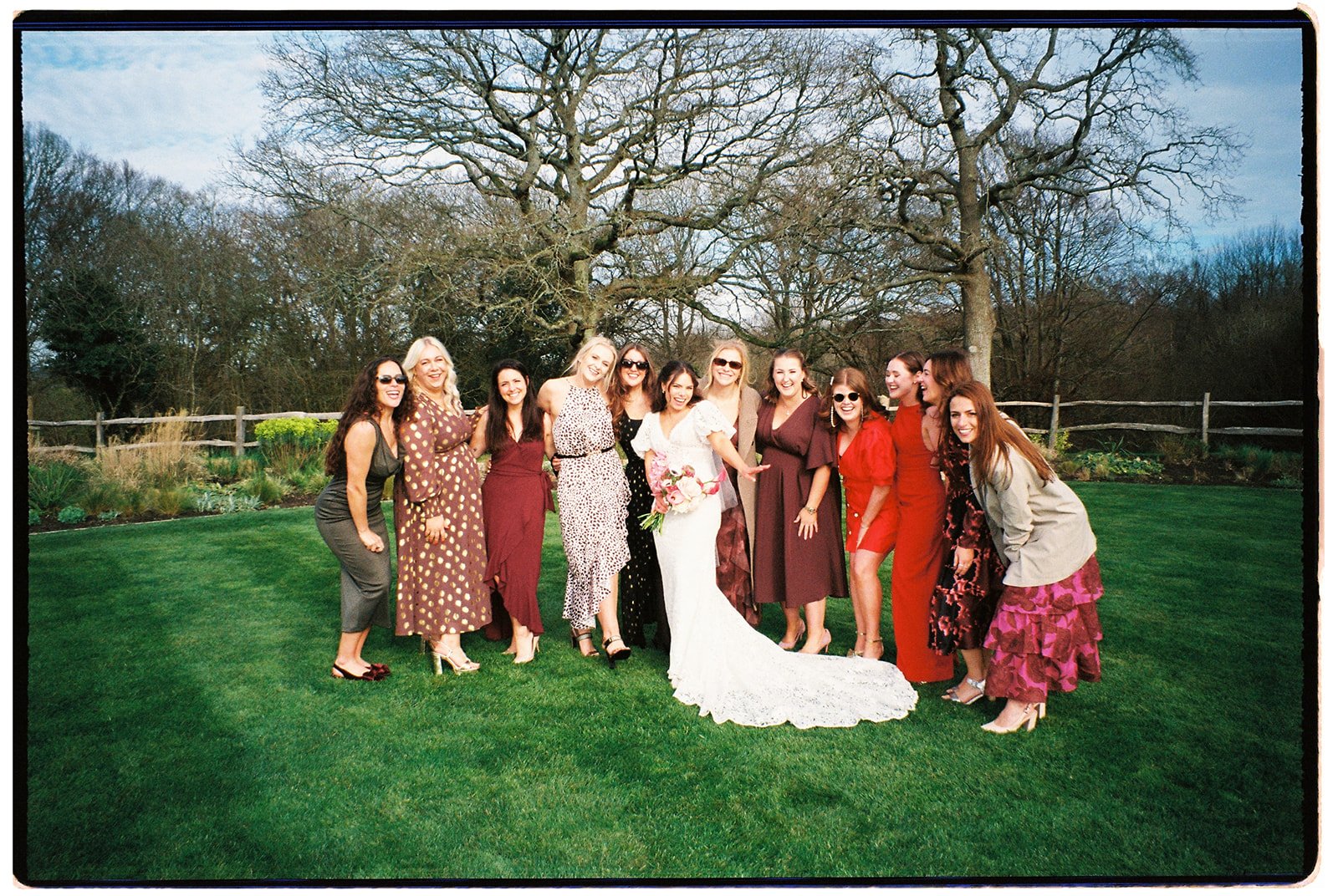 A group of women standing together outdoors on a lawn, with some women wearing sunglasses and all dressed in colorful outfits, posing for a photo.