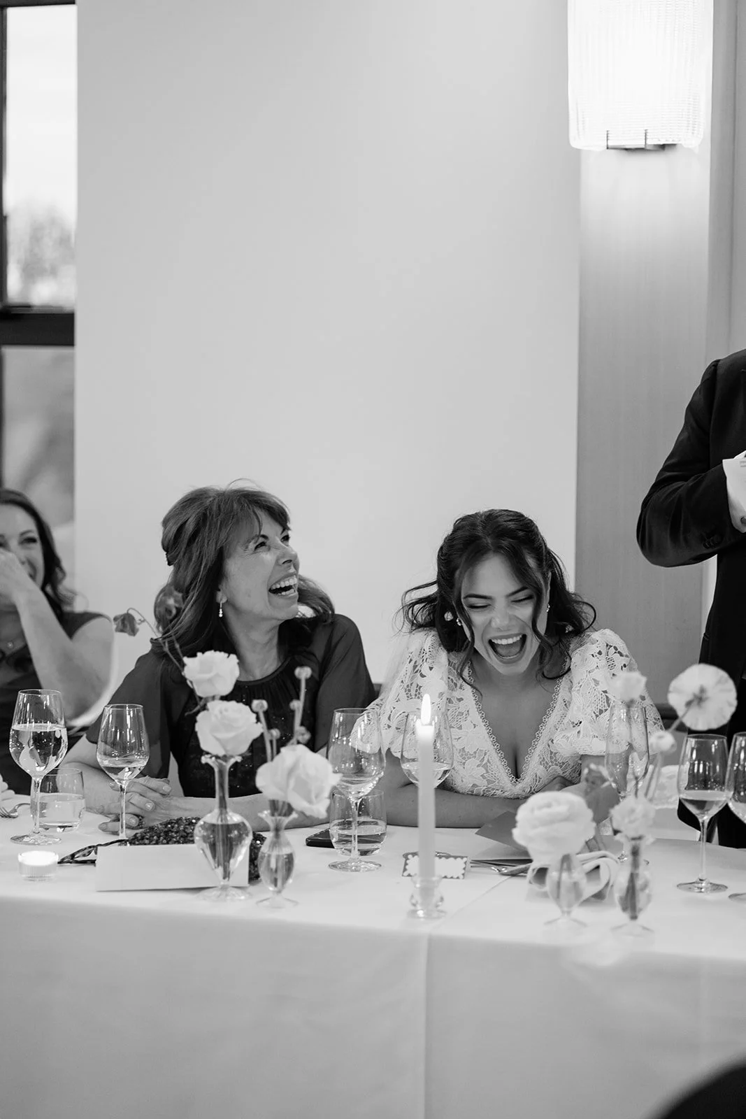 A black and white photo of a women’s wedding reception party, with women sitting at a decorated table laughing and enjoying themselves.