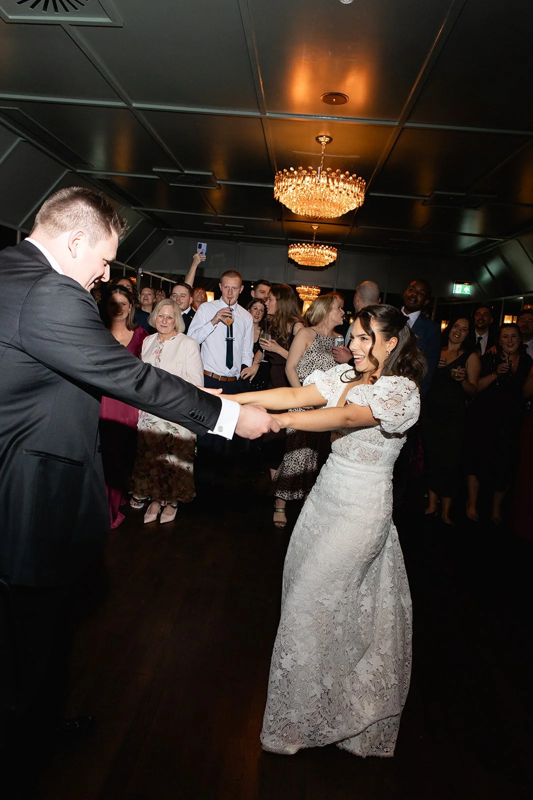 A bride and groom dancing at their wedding reception surrounded by guests.