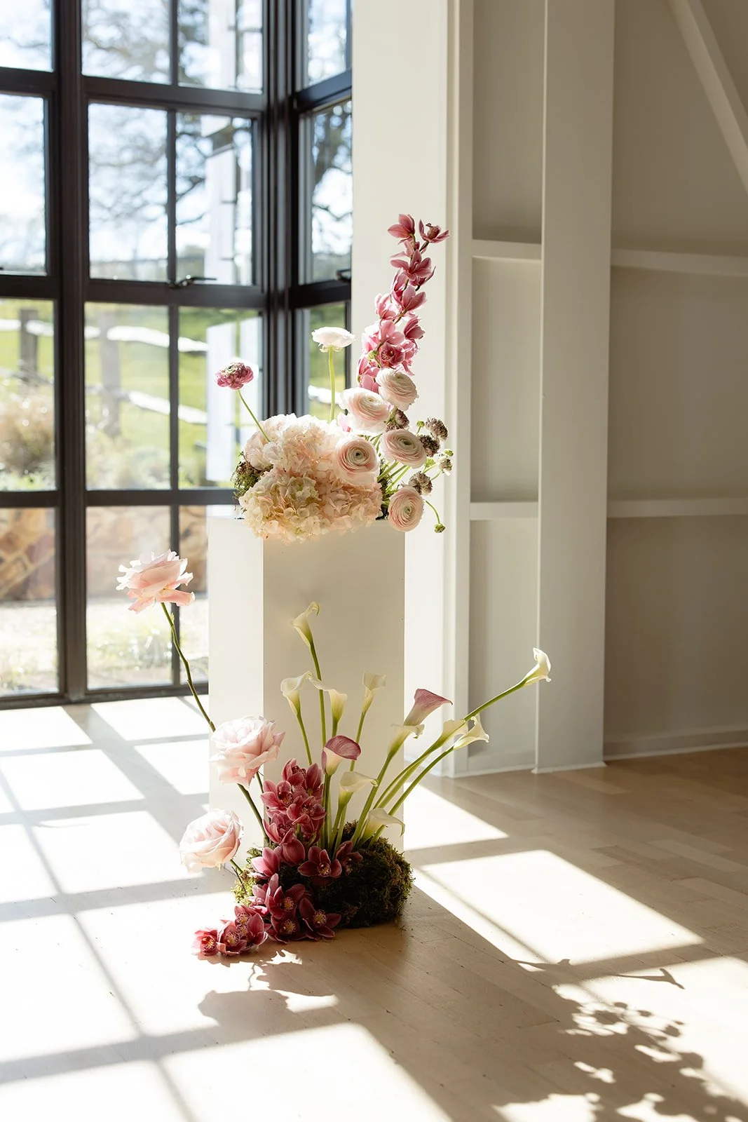 Elegant floral arrangement with pink and white flowers near large window with natural light.