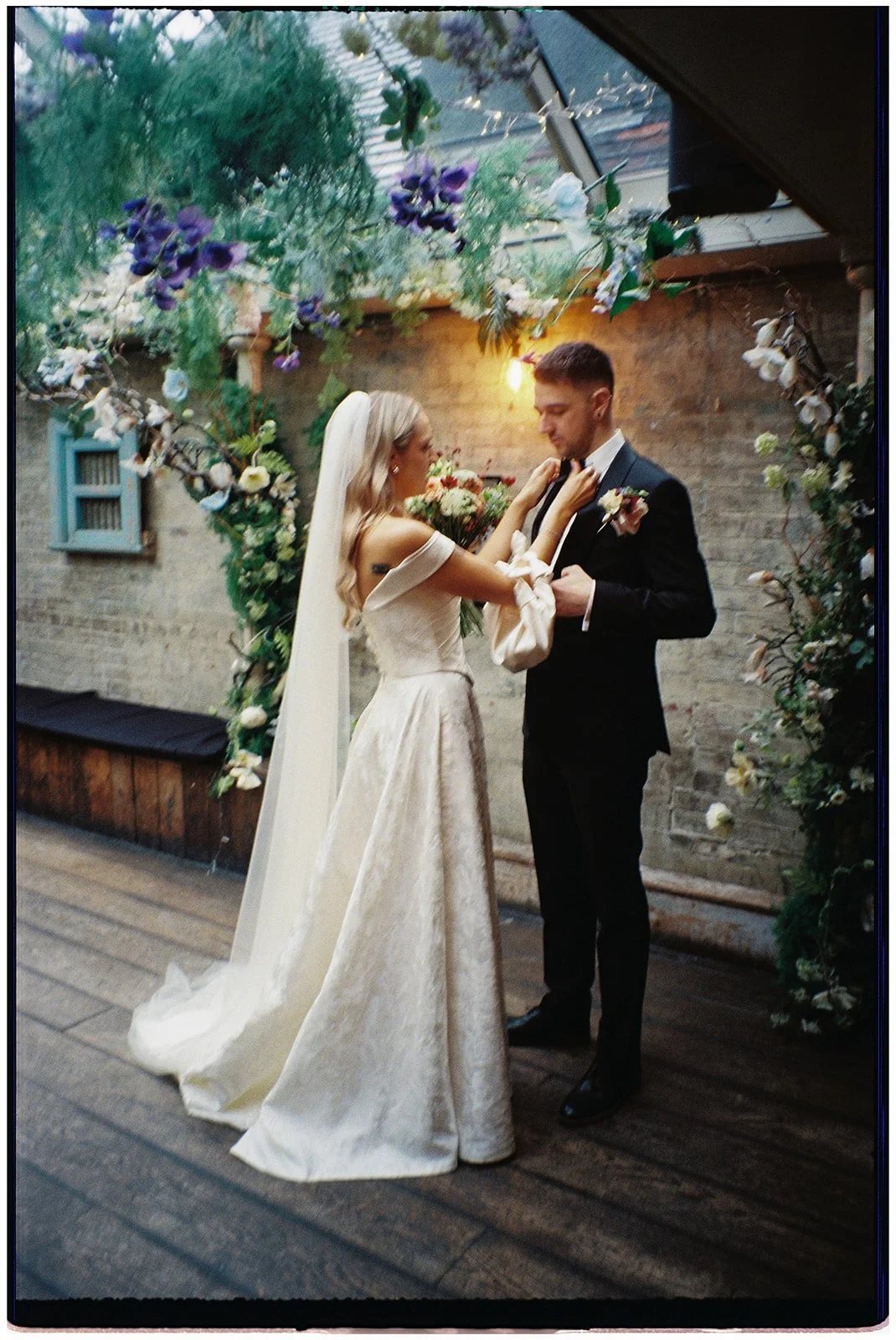 A bride and groom sharing a dance during their wedding ceremony in a decorated indoor venue with floral arrangements and string lights.