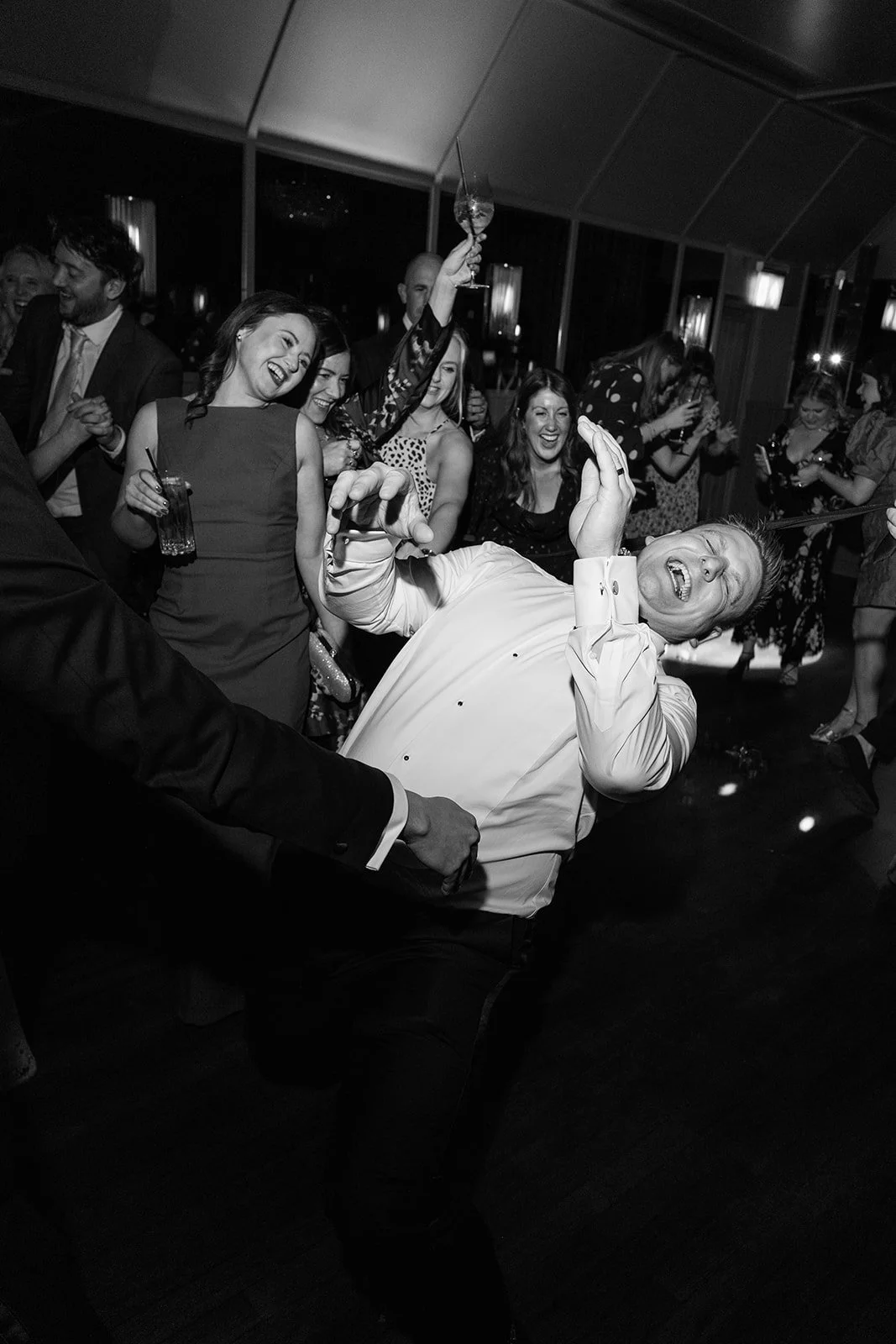 People dancing and celebrating at a party, with a man in a white shirt being lifted or held, appearing to enjoy the moment.