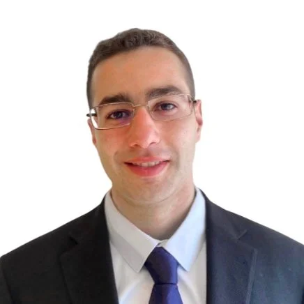 A man in a black suit, white shirt, and dark tie, with glasses, smiling against a white background.