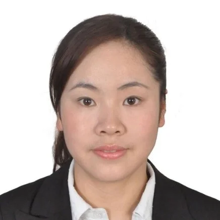 A woman with dark hair wearing a black blazer and white shirt, looking at the camera against a white background.