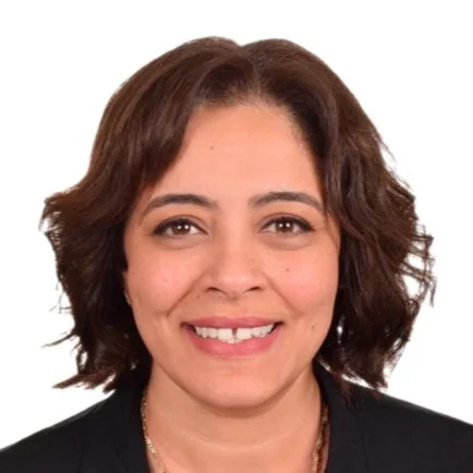 Headshot of a woman with shoulder-length curly brown hair, smiling, wearing a black top, against a white background.