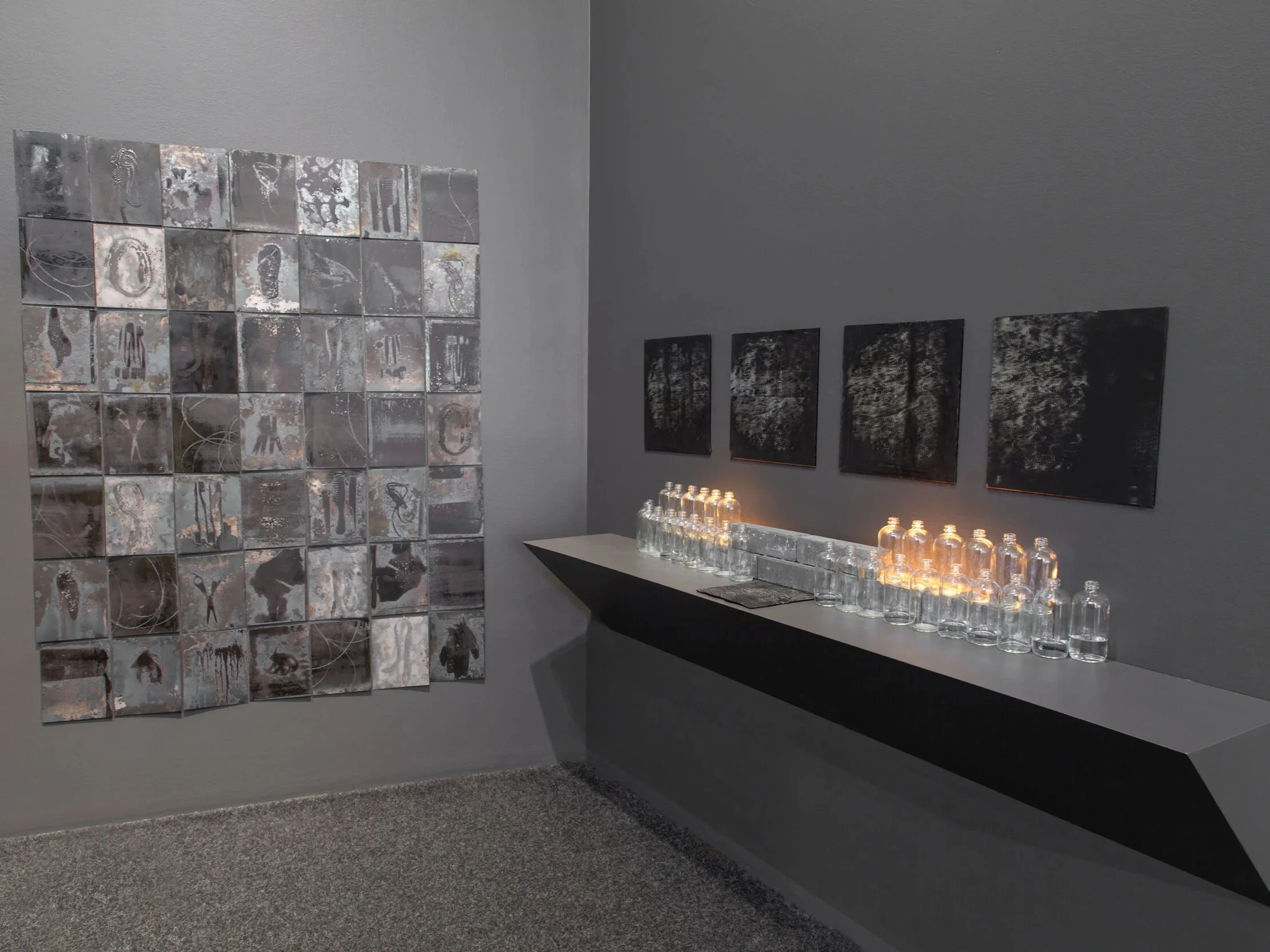 Dispossession, installation by Carrie Iverson featuring glass, prints, found bottles, and cast glass exploring memory, borders, and displacement.