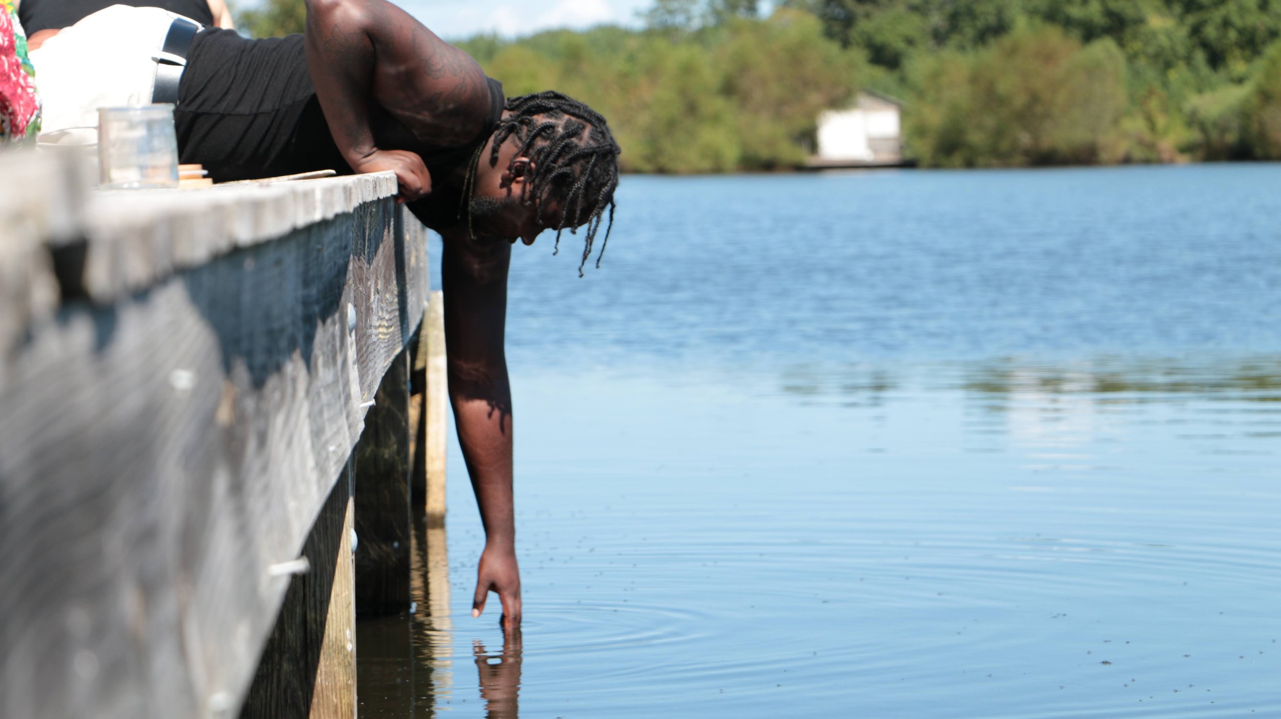 Anesu reached off a dock and dips his hand into the water beneath.