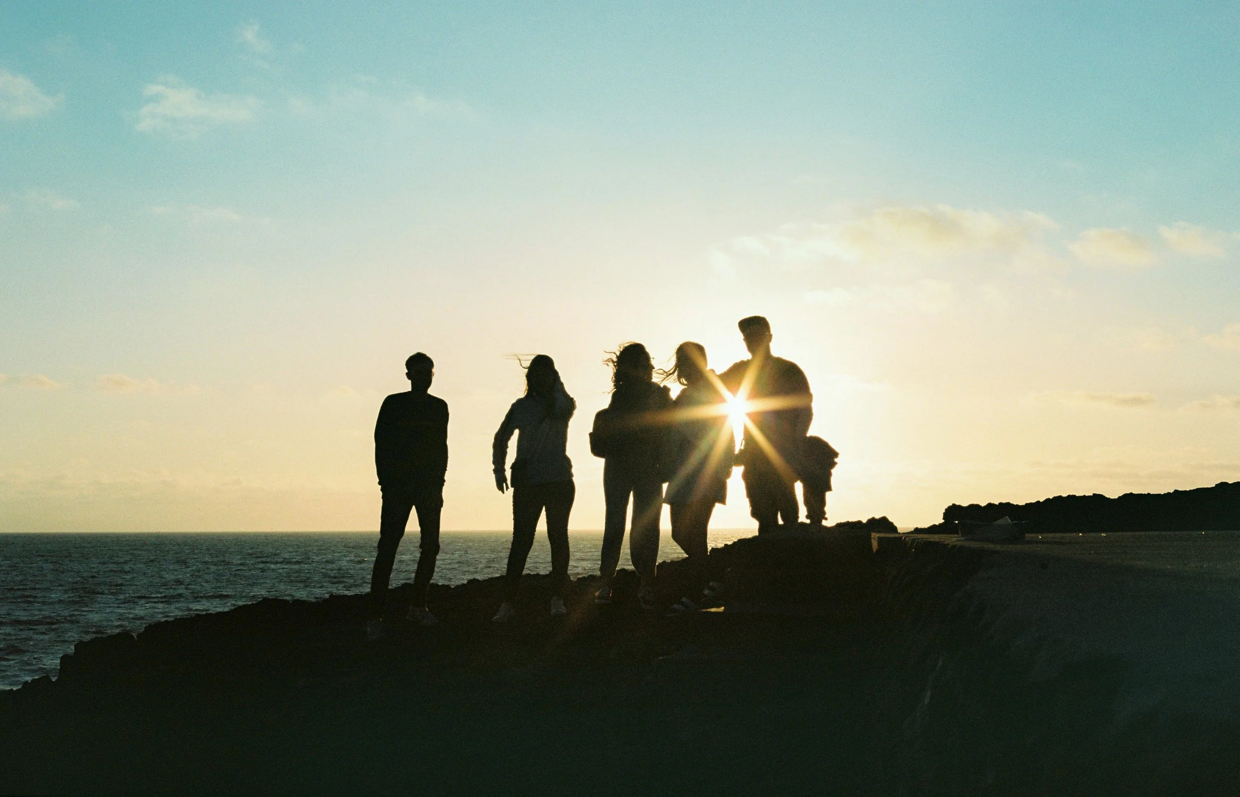 Team standing on shore overlooking the sun set over the ocean